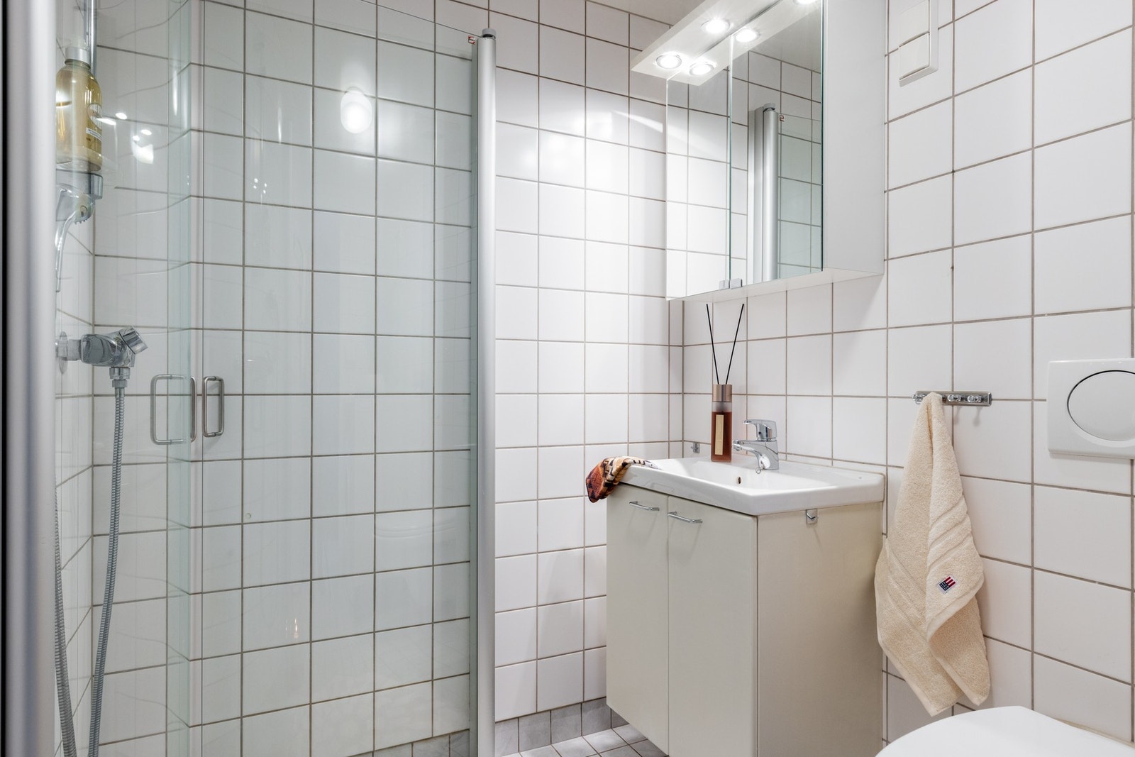 Over servantbenken er det montert et overskap med speil og belysning. Toalettet er veggmontert og i dusjen er det 90*90cm dusjhjørne med innfellbare buede dusjvegger. Galleribilde