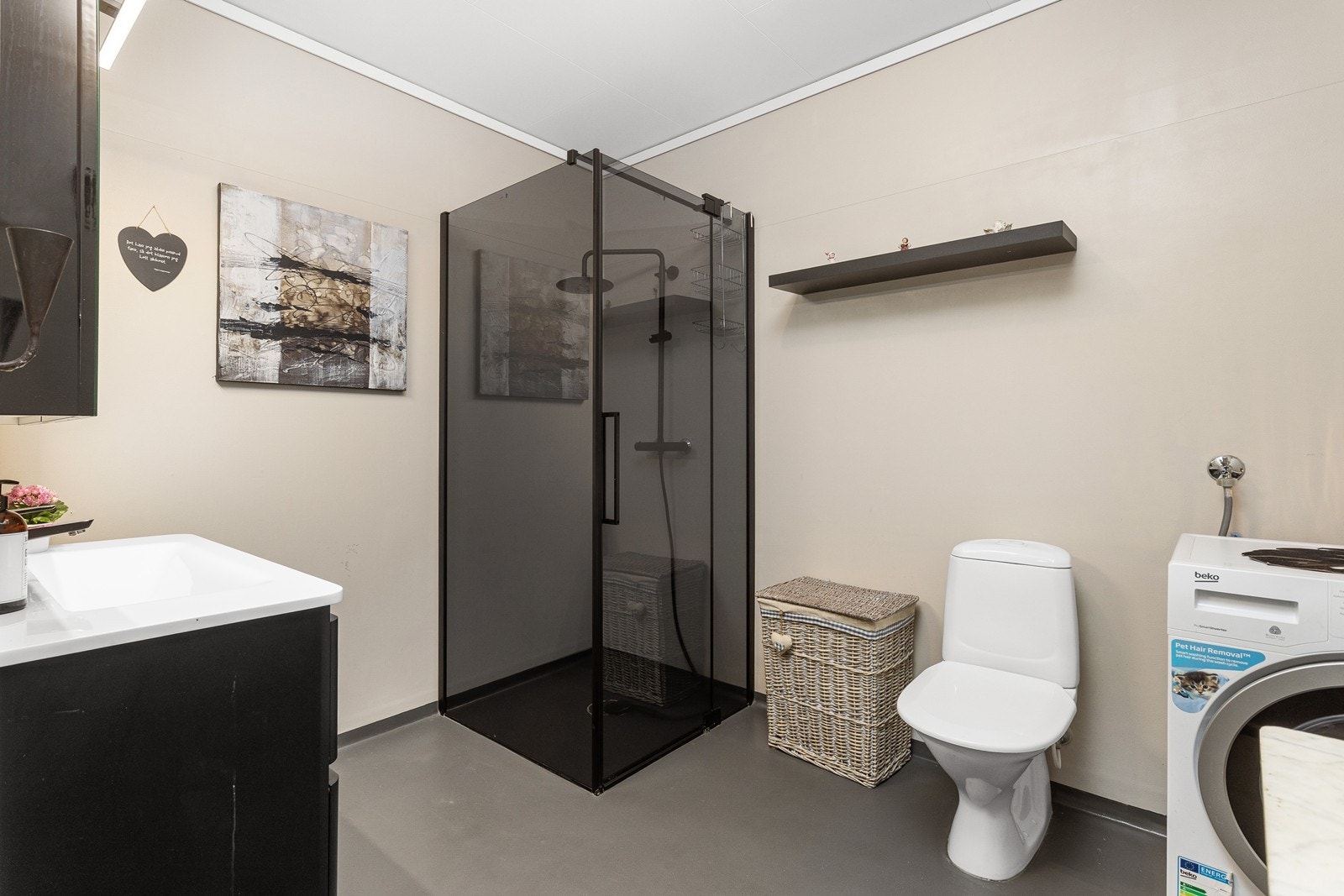 Badet har en moderne baderomsinnredning med heldekkende servant og skuffer, samt speilskap med integrert belysning. Dusjhjørnet har elegante mørke glassvegger og regnfallsdusj. Badet har også toalett og opplegg for vaskemaskin. Galleribilde