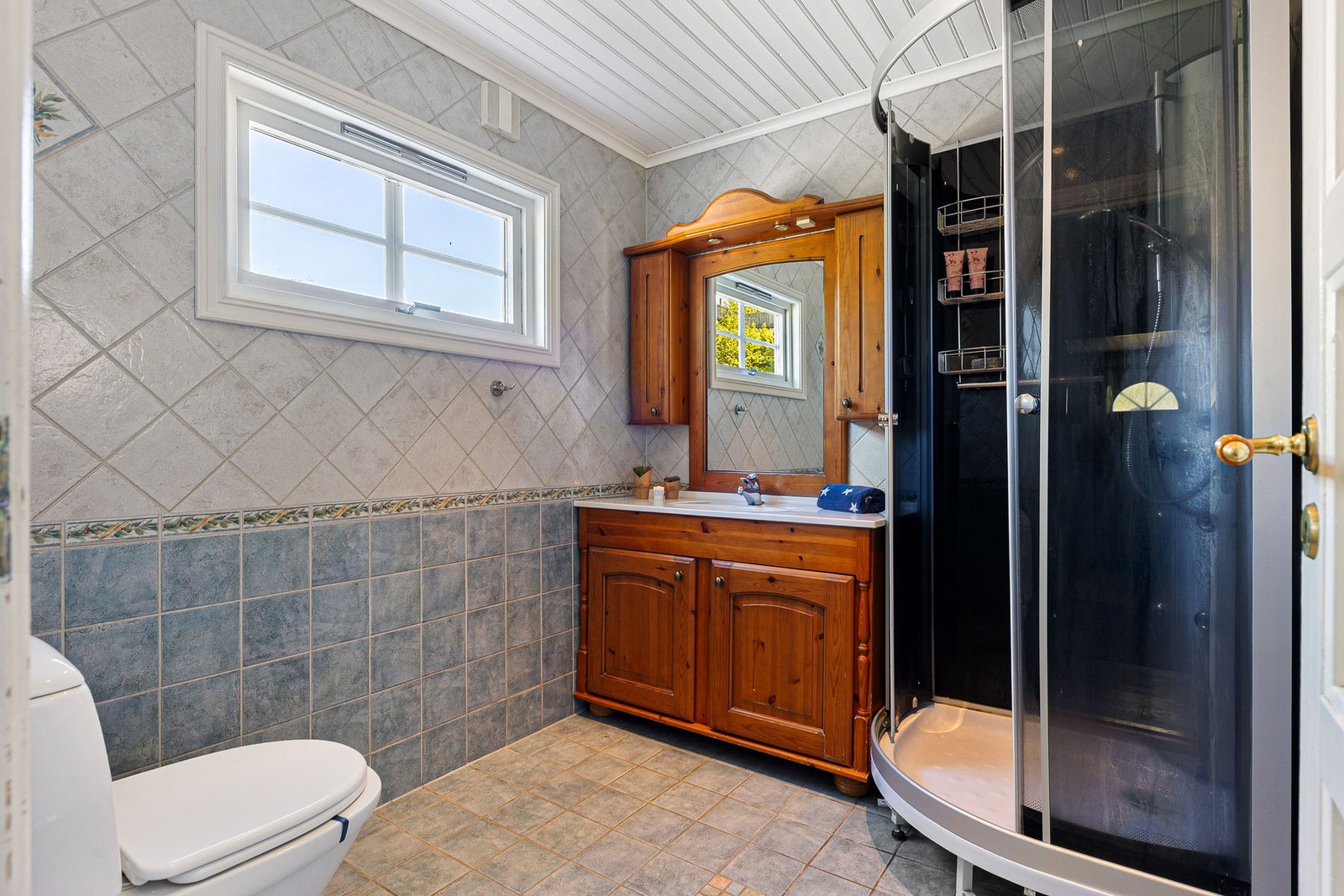 Flislagt og romslig baderom med servant i innredning, dusjkabinett og toalett Galleribilde