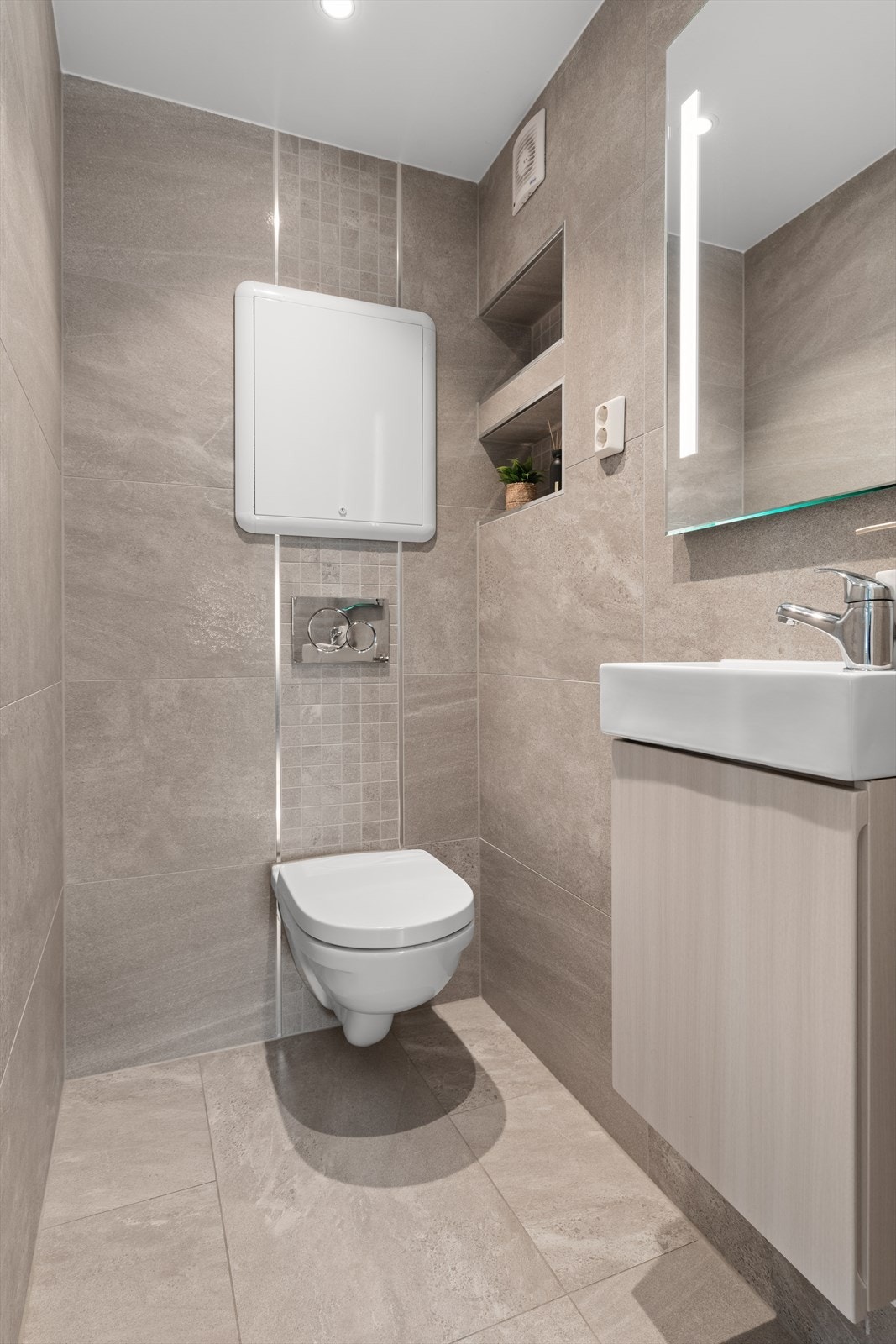 WC har veggfestet toalett, nisje i vegg, servant med underskap og speil over Galleribilde