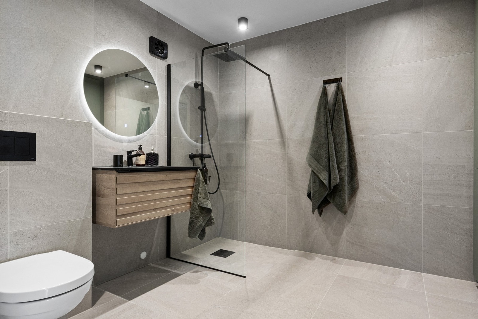 Badet har en god størrelse og ble smakfullt renovert i 2023. Badet er utført med grå fliser på gulv og vegger, varmekabler i gulvet og utenpåliggende downlights i himlingen. Galleribilde