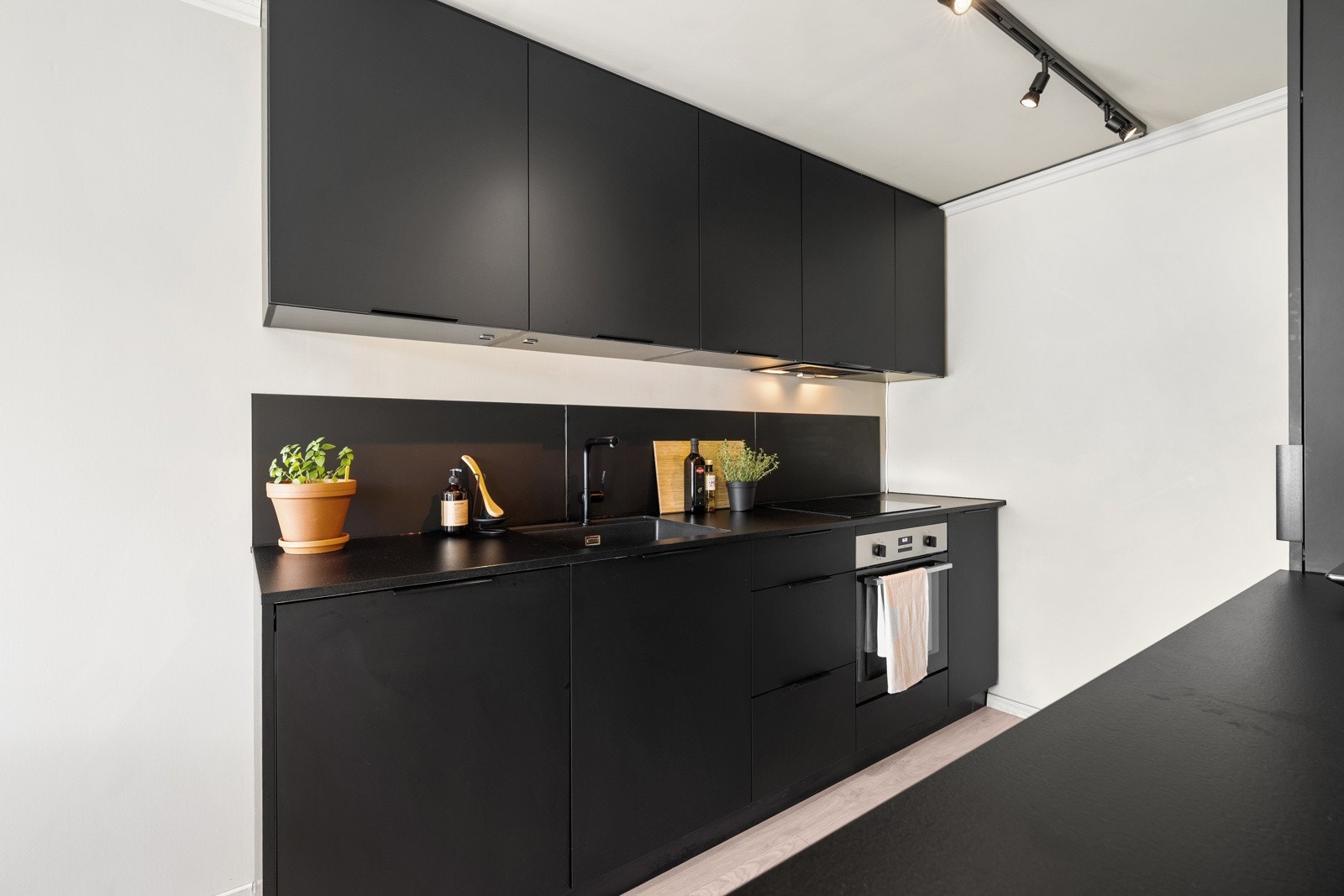 Rålekkert kjøkken med mørke fronter og en mørk benkeplate. Galleribilde