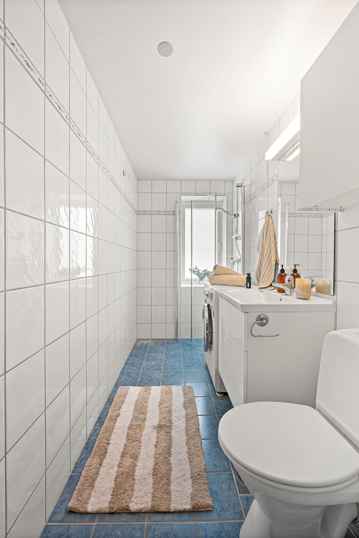 Rommet er innredet med et dusjhjørne med glassdører, gulvmontert toalett og en servant med speil. Galleribilde