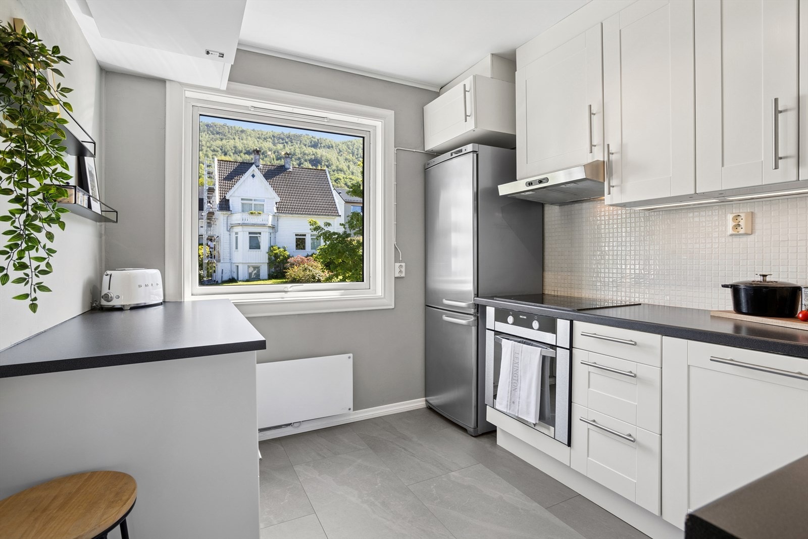 Kjøkkenet har utmerket skap- og benkeplass. Den tidløse kjøkkeninnredningen har hvite fronter, integrerte hvitevarer, laminat benkeplate og mosaikkfliser over deler av benkeplaten. Galleribilde