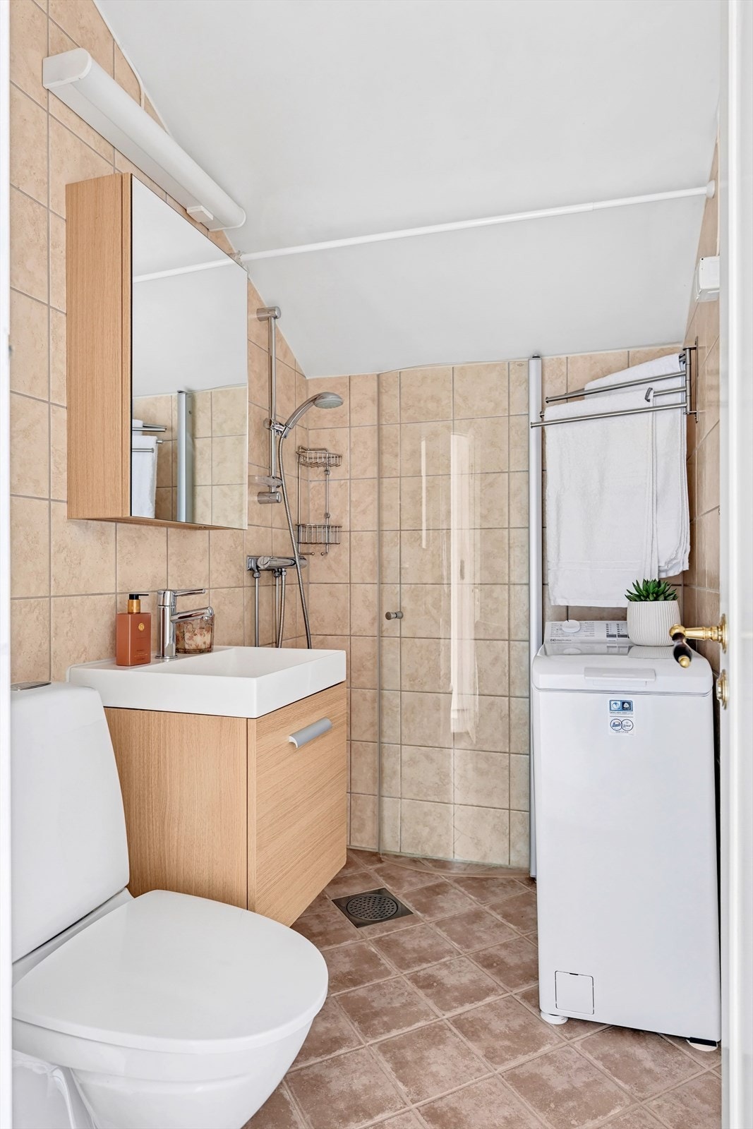 Pent flislagt bad bestående av frittstående wc, servant med underskap, overskap med speilfronter, inn-/utadslående dusjdør, og mulighet for forheng mot innredning Galleribilde