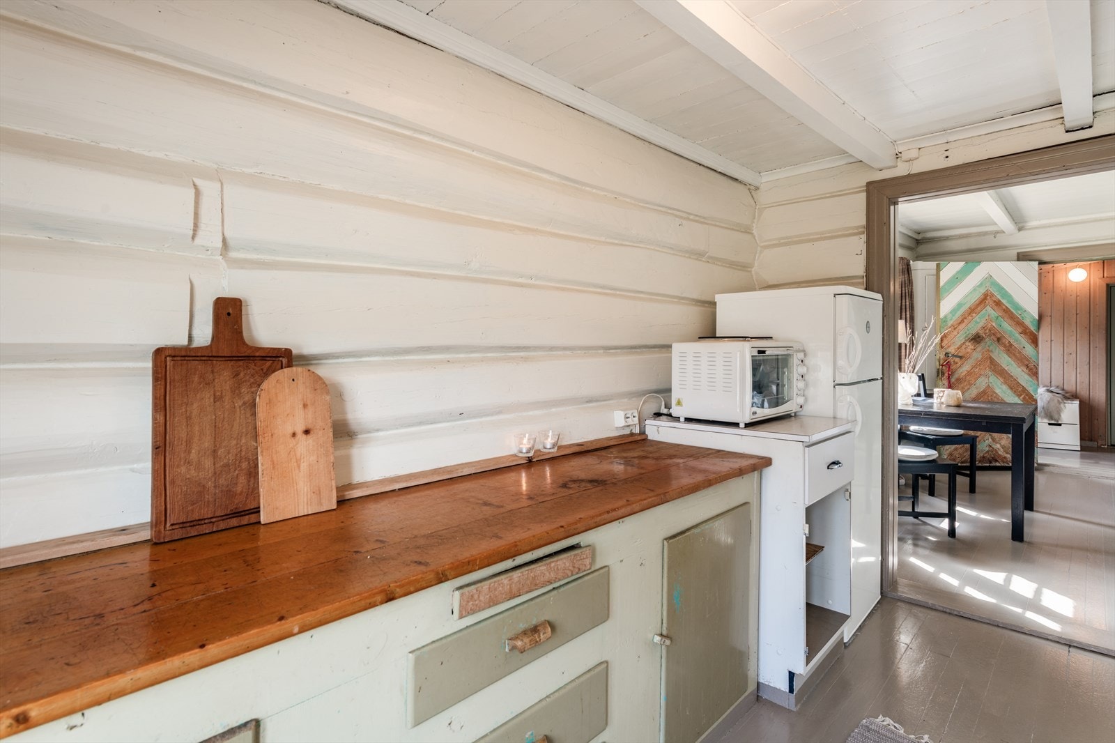 Enkel, eldre kjøkkenbenk, hybelkomfyr og kjøl-/fryseskap. Galleribilde