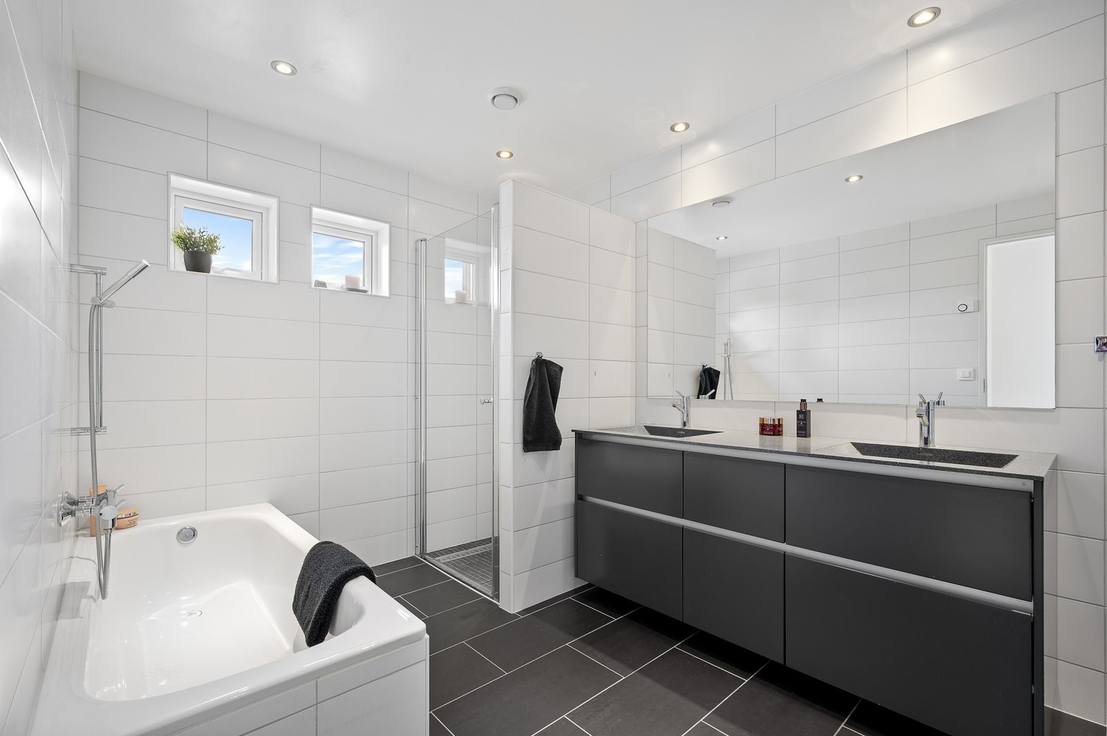 Lekkert bad med dusjhjørne, veggmontert WC, Vannbåren/elektrisk håndkletørker, dobbelvask og badekar. Galleribilde