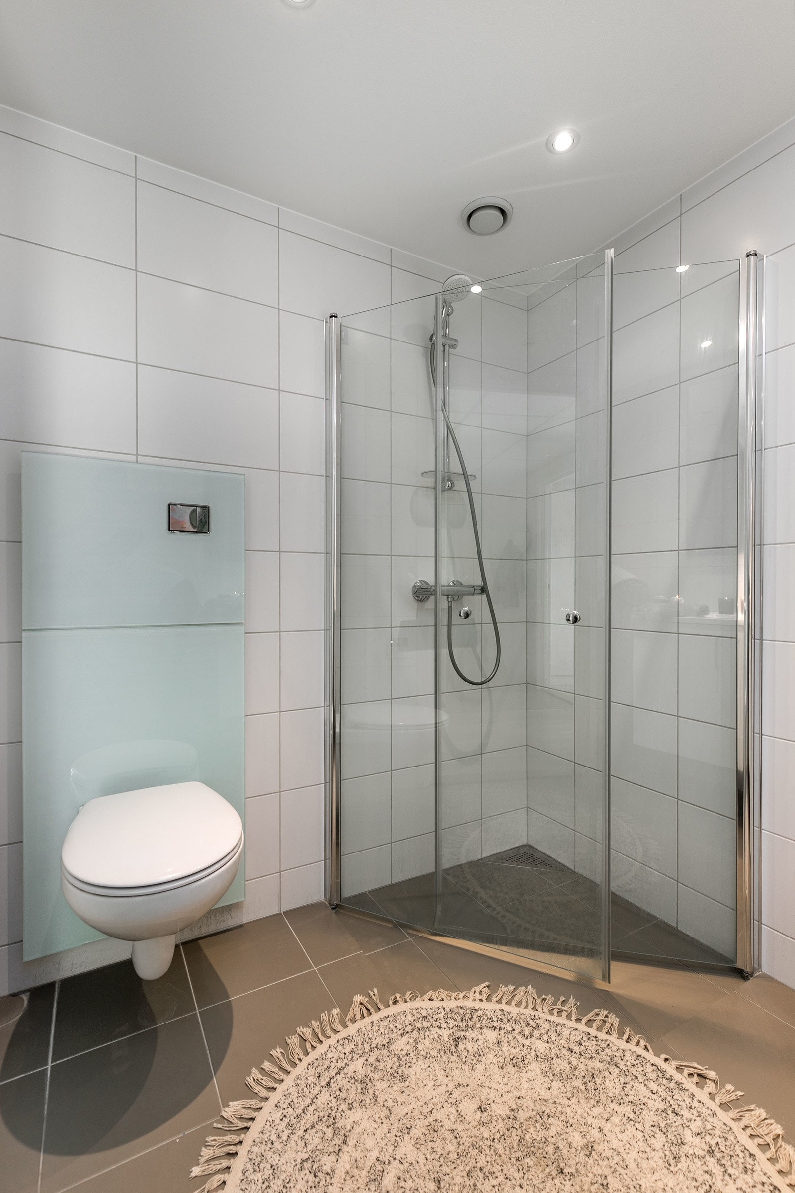Videre har badet et nedsenket dusjhjørne med innfellbare glassdører og hånddusj. Rommet har opplegg og plass for både vaskemaskin og tørketrommel i vaskesøyle. Himlingen er pent lyssatt med downlights. Galleribilde