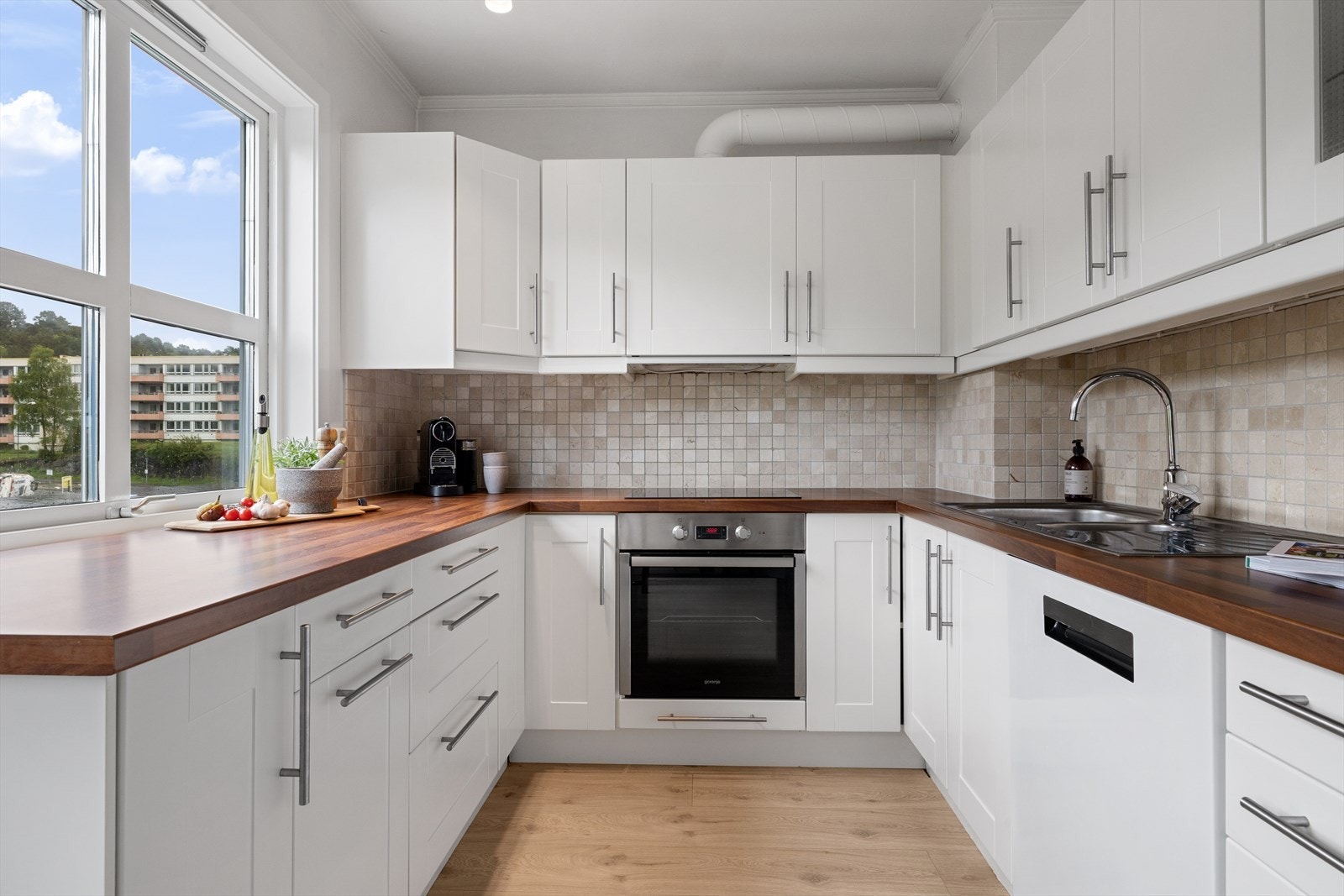 Flott kjøkken med hvite profilerte fronter og mosaikkfliser mellom over- og underskap. Galleribilde