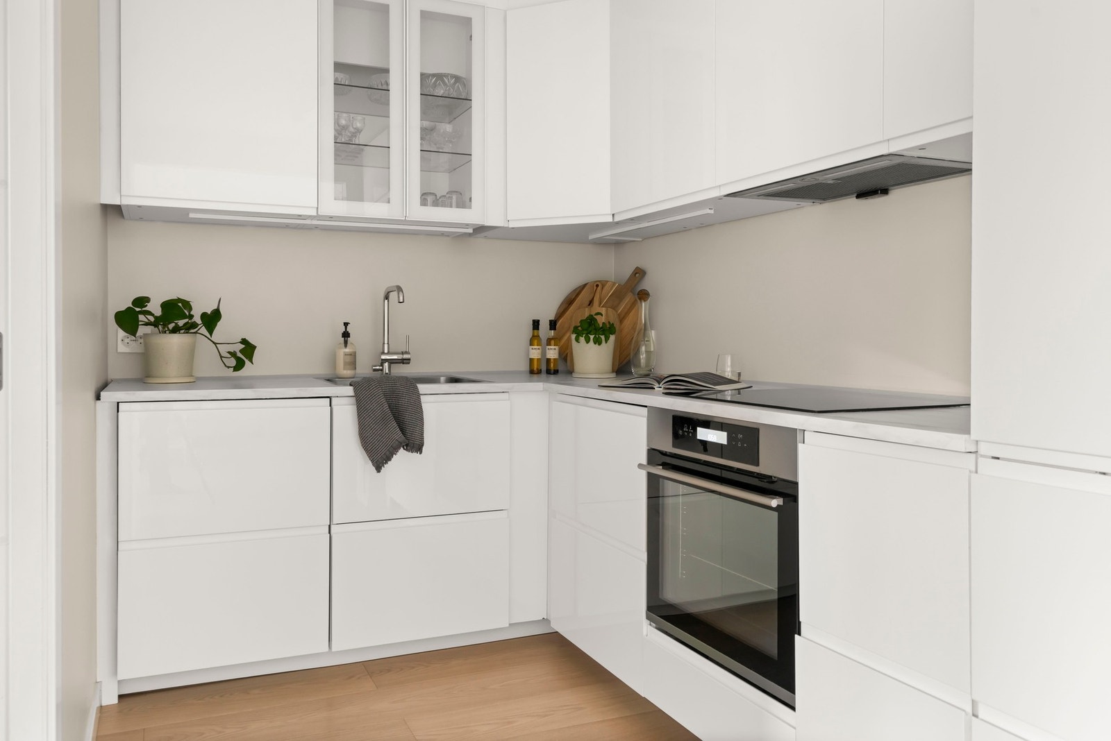 Stilren kjøkkeninnredning fra 2023 med slette fronter, benkeplate av laminat med nedfelt oppvaskkum og et overskap med innfelt glassfelt og innebygget belysning. Galleribilde