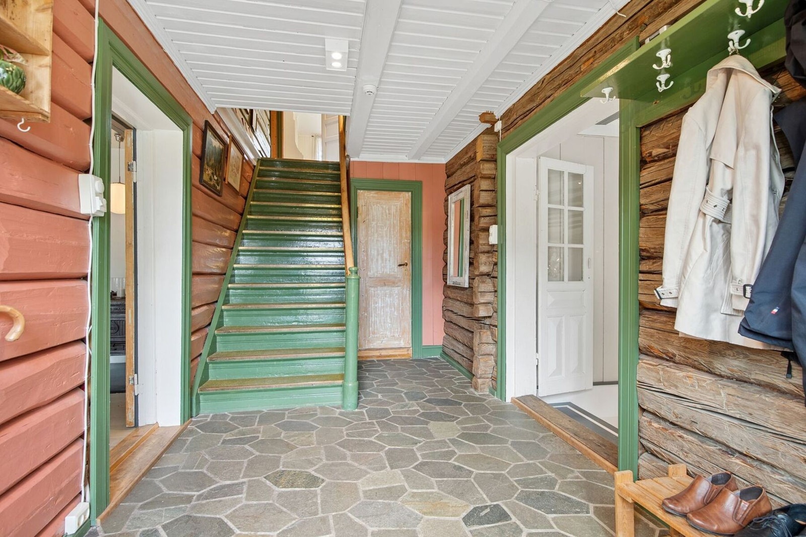 Inne venter en romslig hall og entré med skiferfliser og elektrisk gulvvarme. Vegger og himling er holdt i malt panel og tømmer. Galleribilde