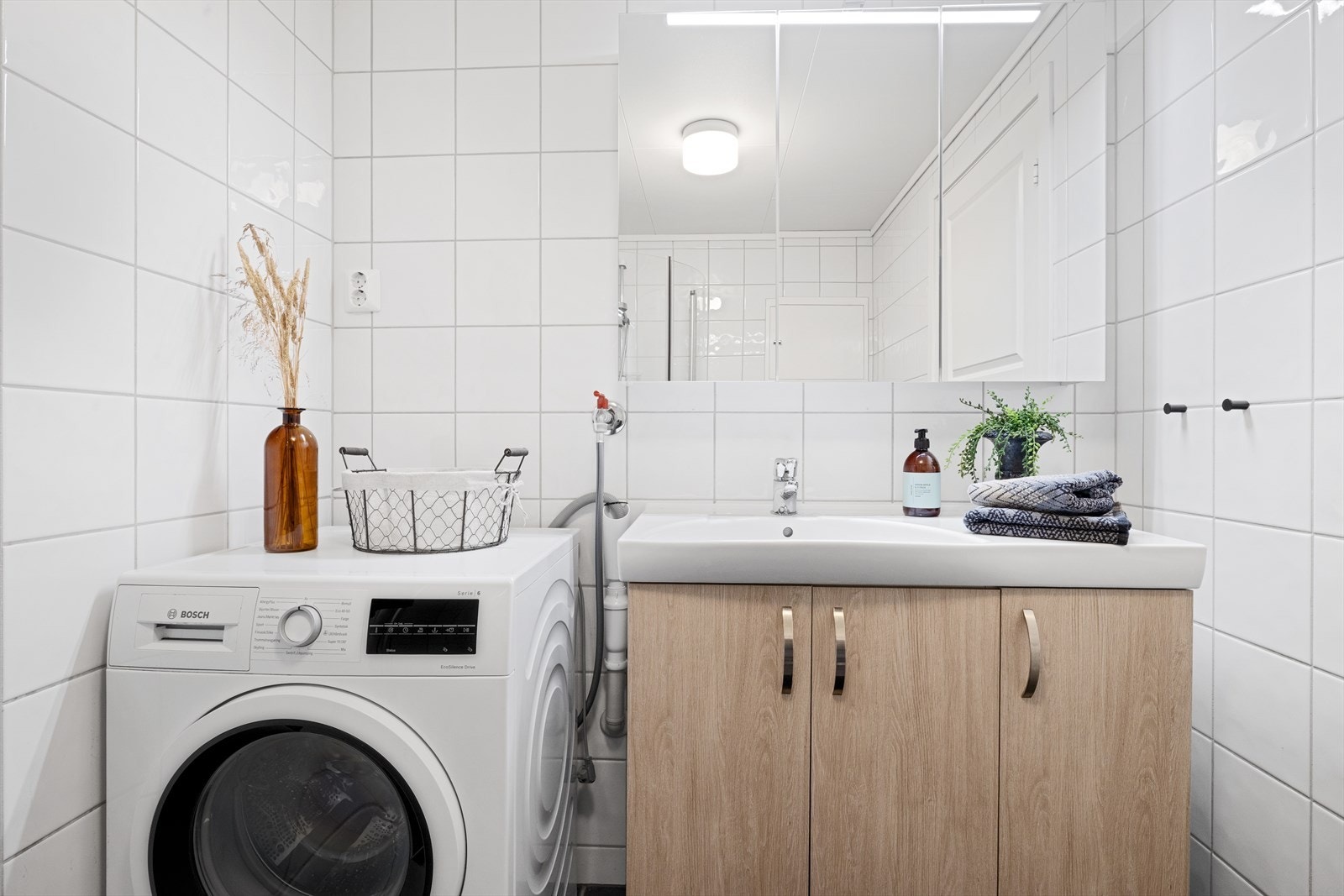 Badet er innredet med toalett, dusjhjørne, benkeskap med servant og speil med belysning over. Plass til vaskemaskin. Galleribilde