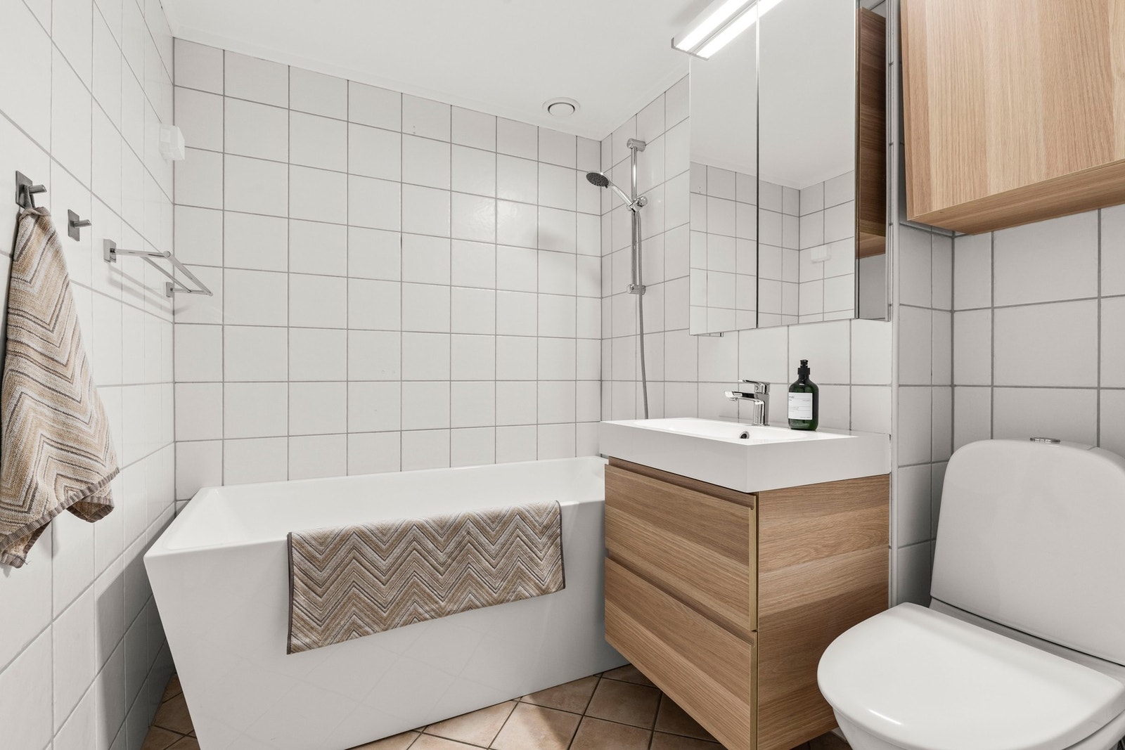 Stilrent flislagt bad med gulvvarme og badekar med dusj. Galleribilde