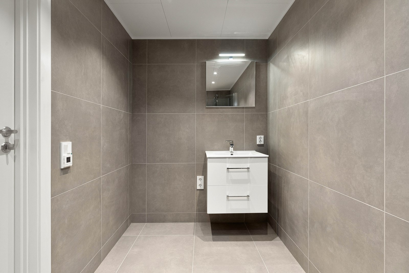 Badet er utstyrt med dusj, vegghengt toalett, servant med innreiing og opplegg for vaskemaskin. Galleribilde