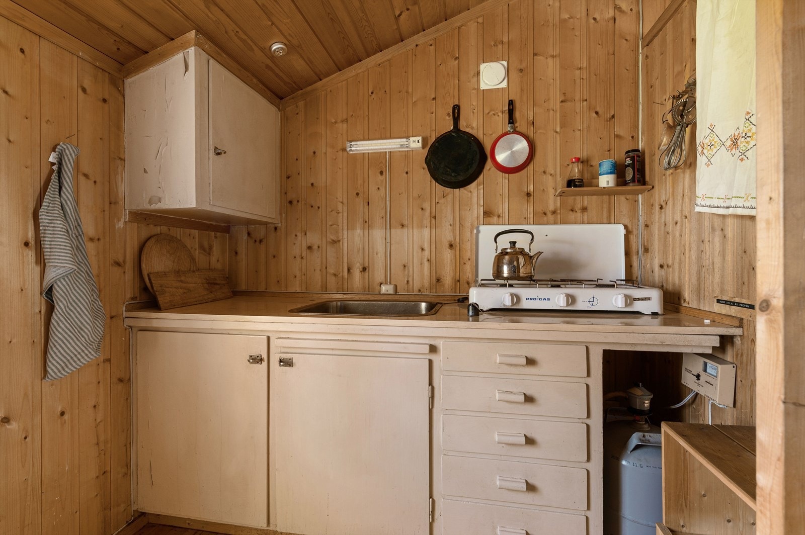 Eldre og plassbygd innredning med heltre skrog og finerte fronter. Laminert benkeplate med nedfelt servant. Eget rom for gassbeholder til koketopp med 3 gassbluss. Galleribilde