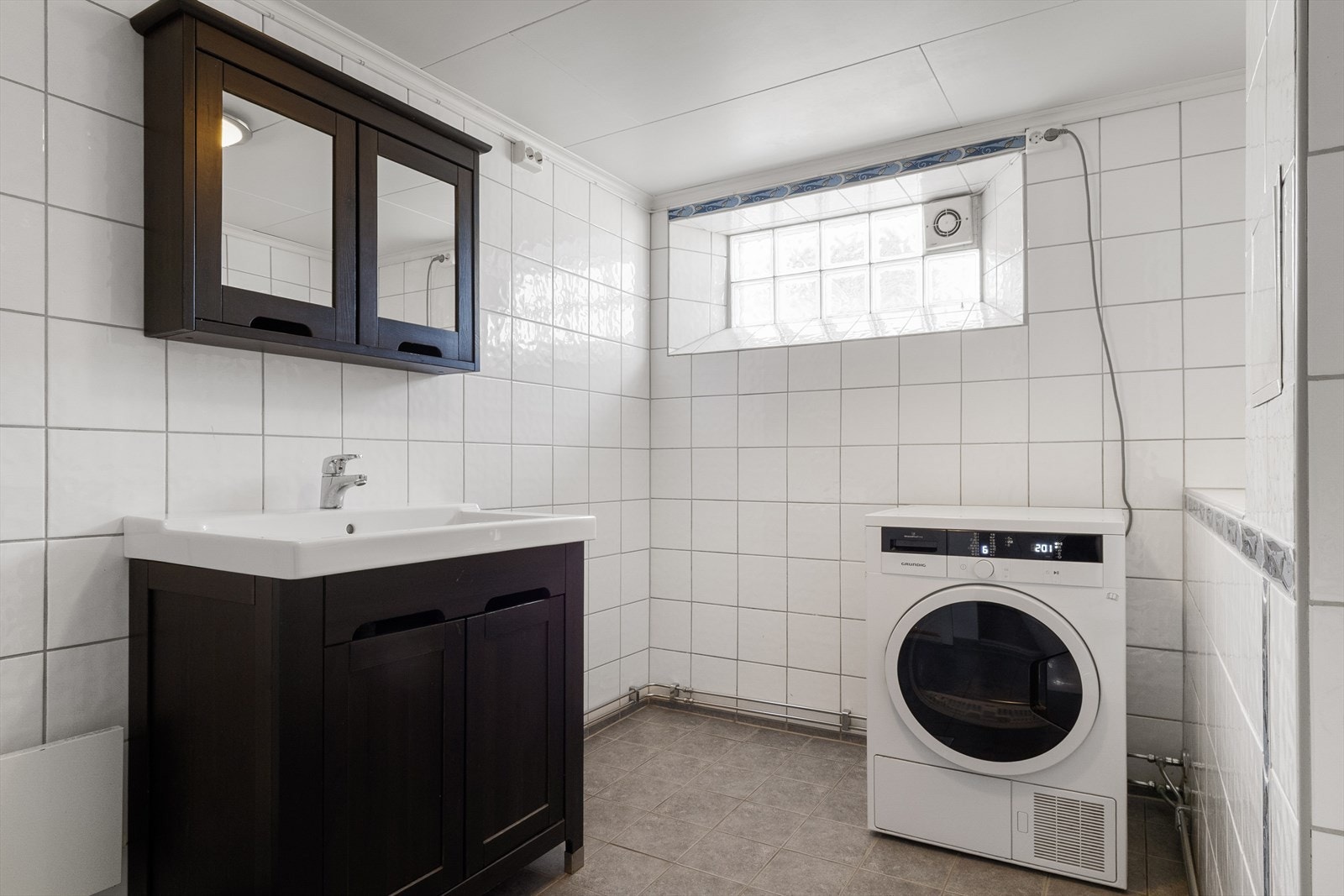 Badet har innredning med servant, gulvmontert toalett og vegghengt dusj med muligheter for dusjforheng - oppvarmes via varmekabler i gulv og vegghengt panelovn. Galleribilde