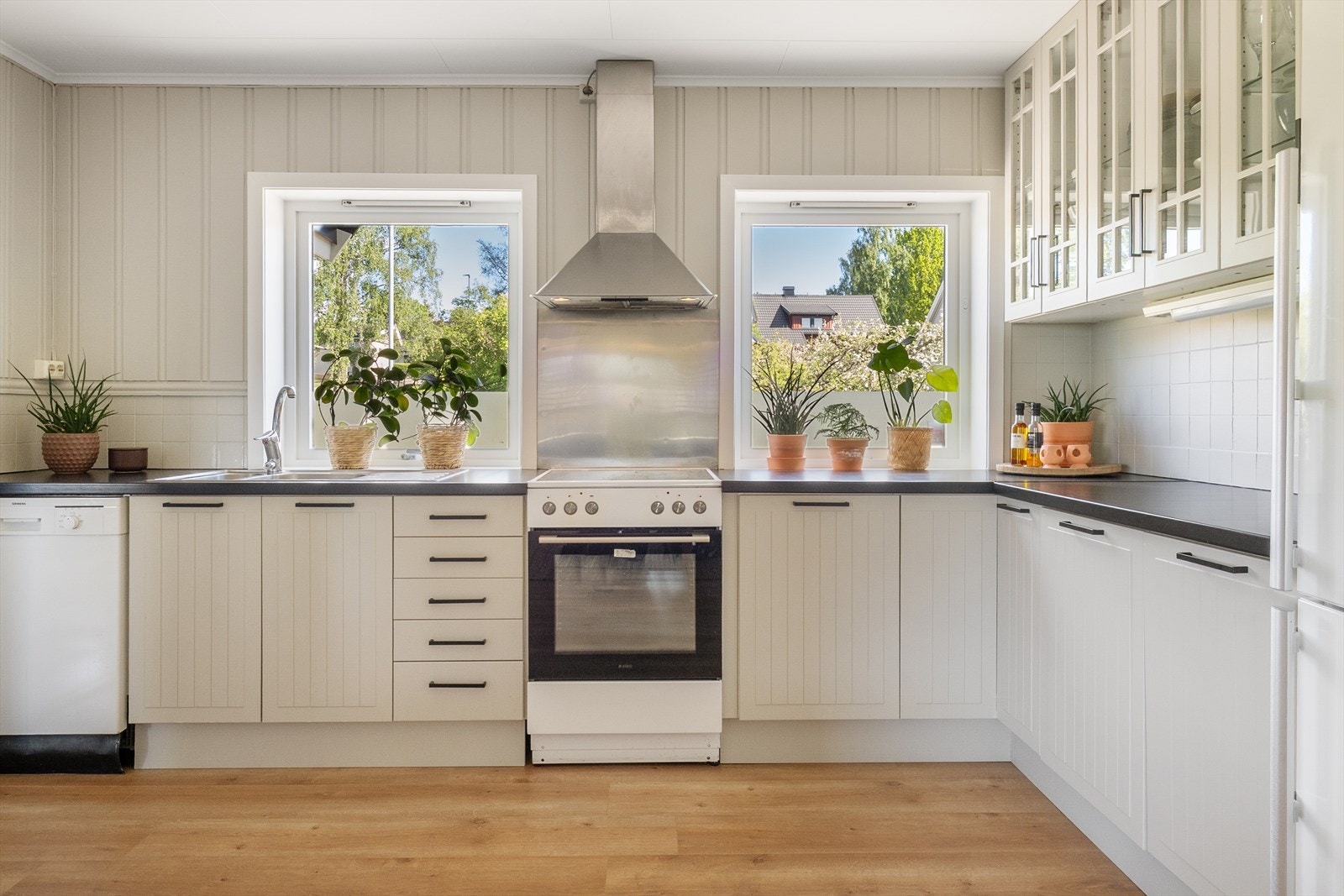 Pen innredning med malte og profilerte fronter. Overskap med glassdører. Laminert benkeplate med nedfelt vaskekum. Overmalte fliser på vegg over benkeplate og stålplate på vegg over kokesone. Galleribilde