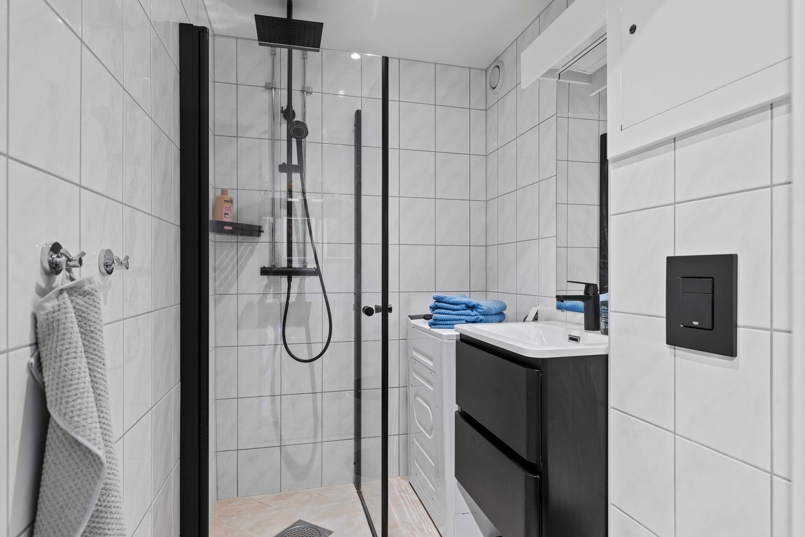 Badet er innredet med en moderne servant med slette fronter, veggmontert toalett, dusjhjørne og opplegg for vaskemaskin Galleribilde