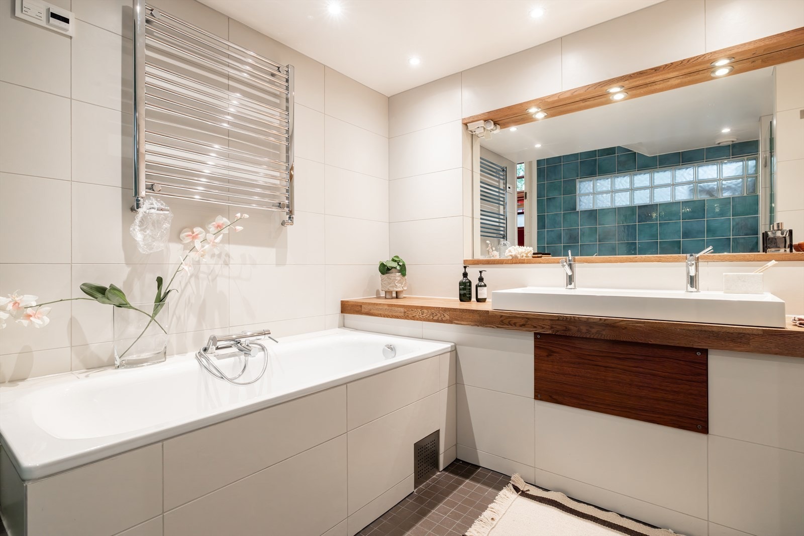 Badet er innredet med gulvstående toalett, servant med underskap, innmurt badekar og dusjsone med svingbare dører. Galleribilde