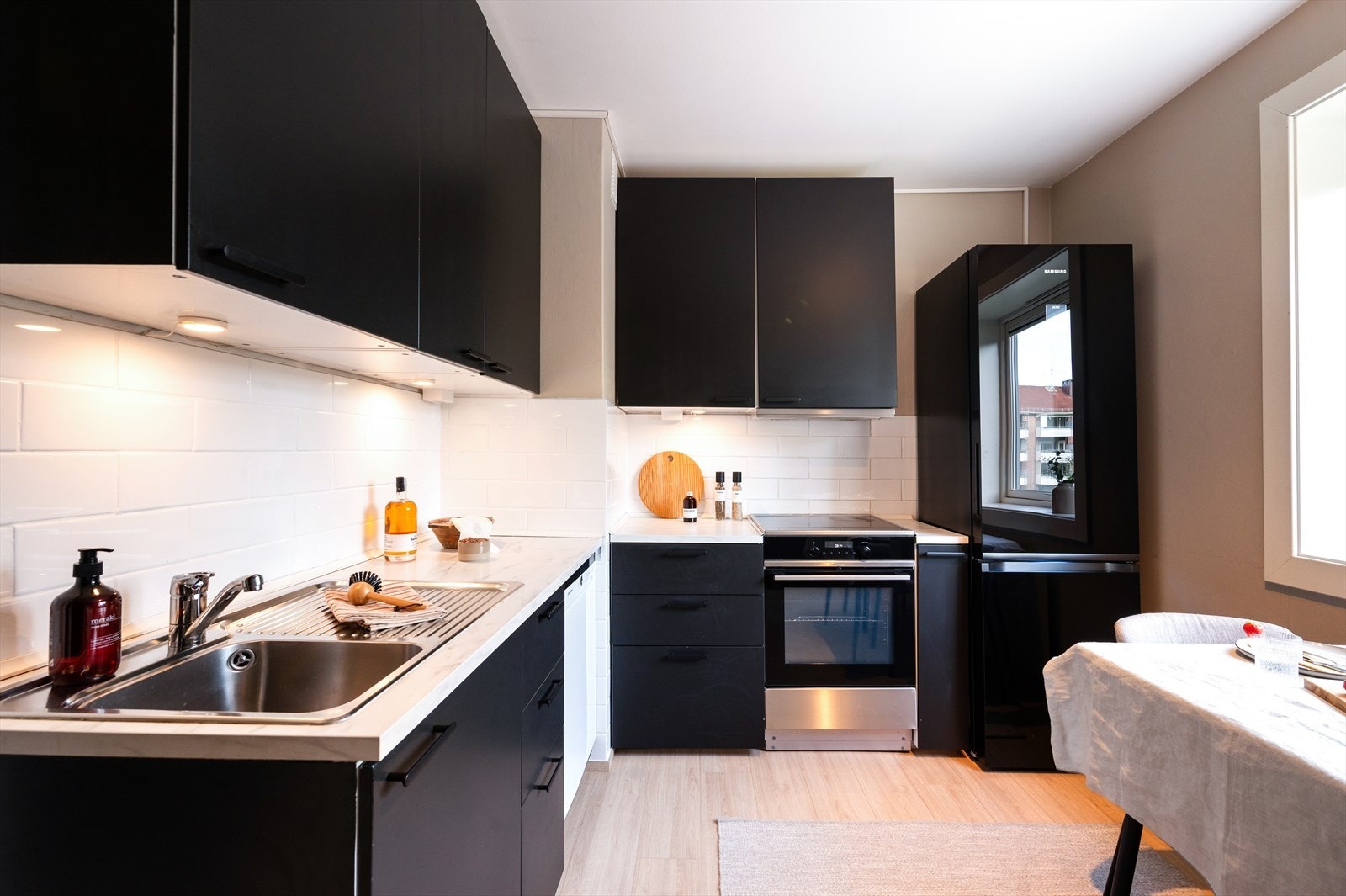 Mørk innredning fra 2019 med glatte fronter som gir et elegant uttrykk, mens den laminert benkeplaten med integrert kjøkkenkum skaper en sømløs og praktisk arbeidsflate. Galleribilde