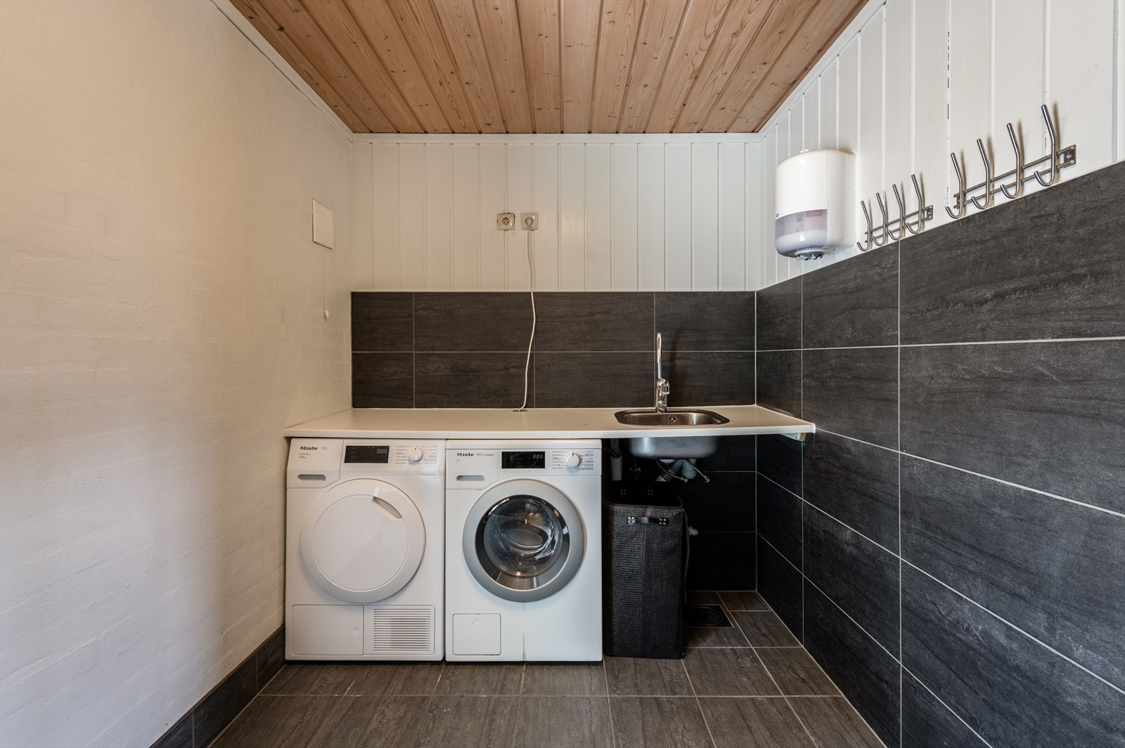 Praktisk vaskerom innredet med benkeplate med nedfelt vask. Det er opplegg for både vaskemaskin og tørketrommel. Galleribilde