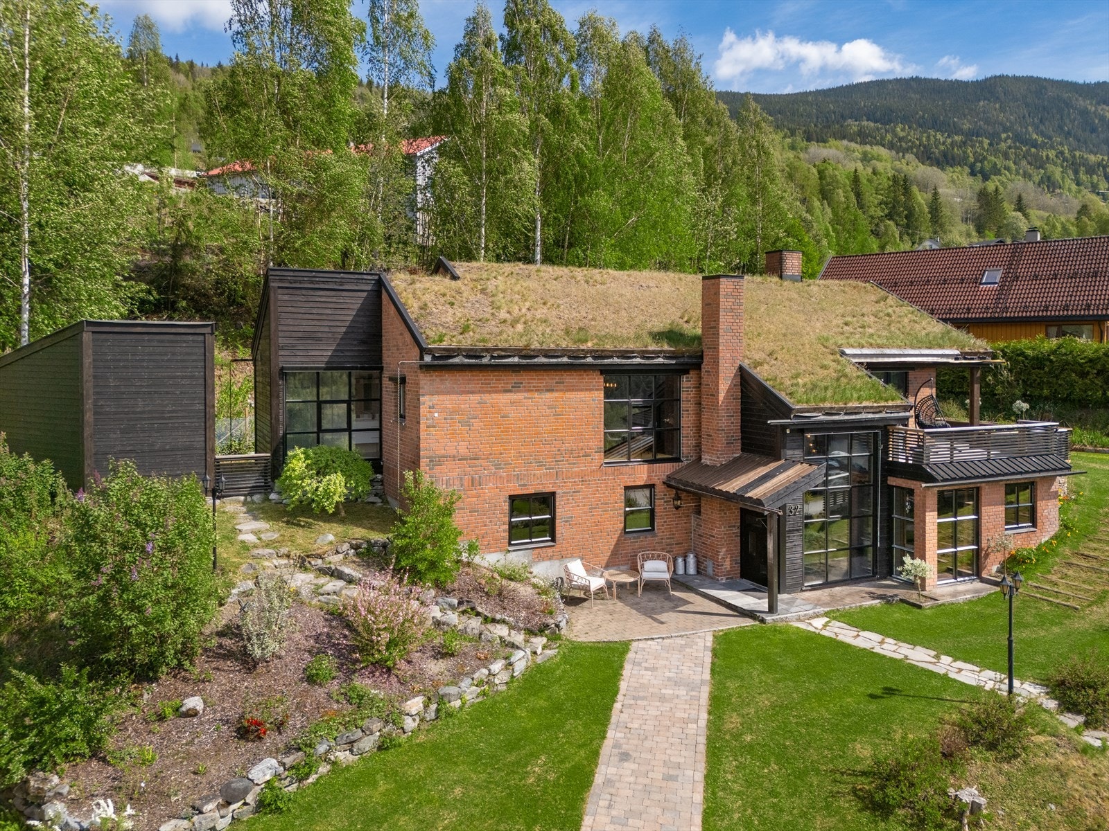 Tomten er pent opparbeidet med plen, beplantning, brostein og naturstein. Galleribilde