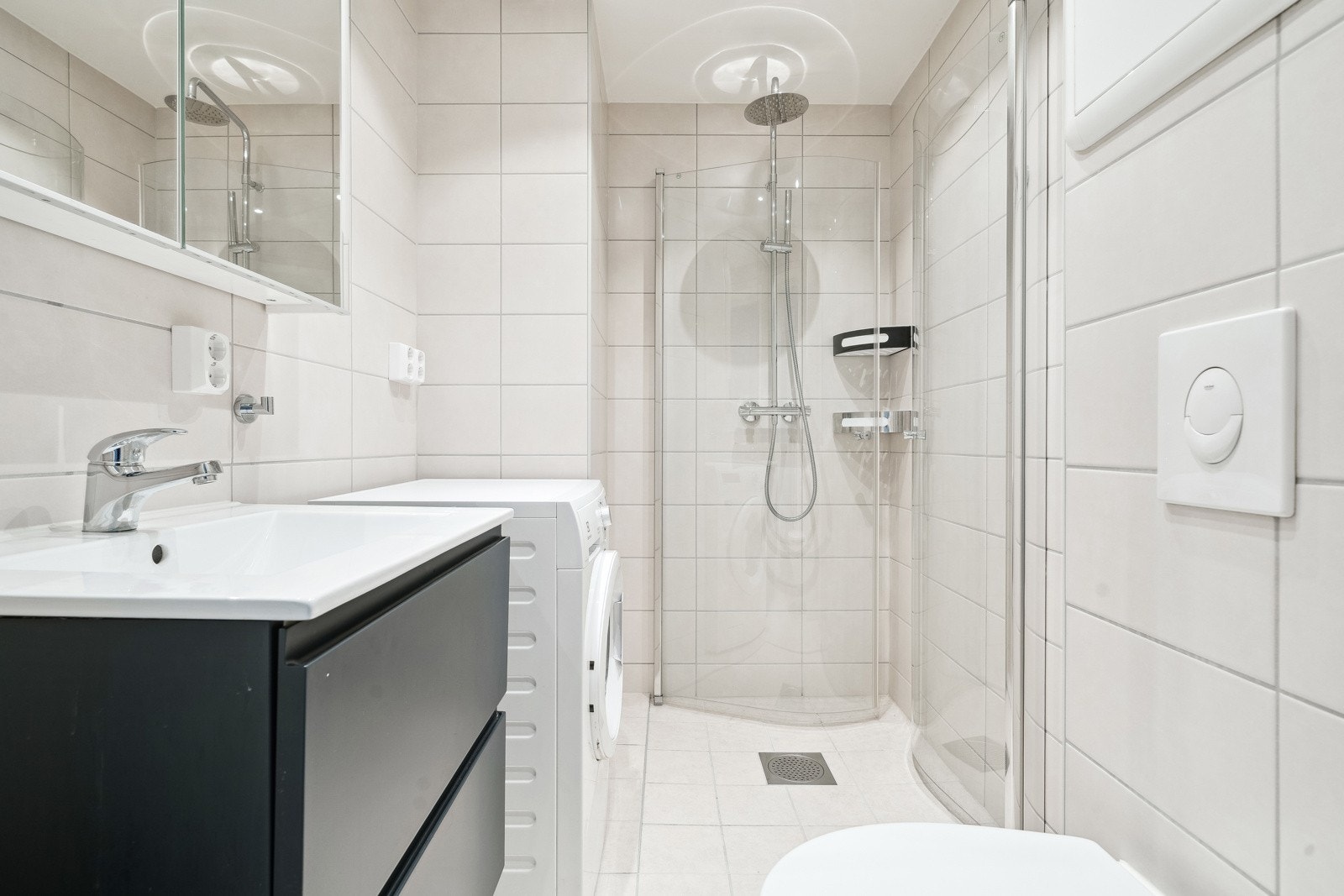 Dusjhjørne med innfellbare buede glassdører samt opplegg for vaskemaskin. Galleribilde