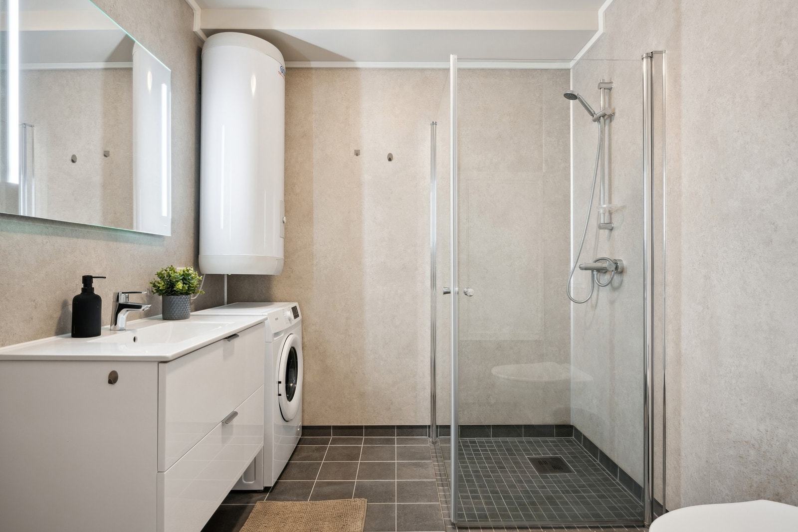 Badet er utstyrt med baderomsinnredning, dusjplass, toalett og opplegg for vaskemaskin Galleribilde