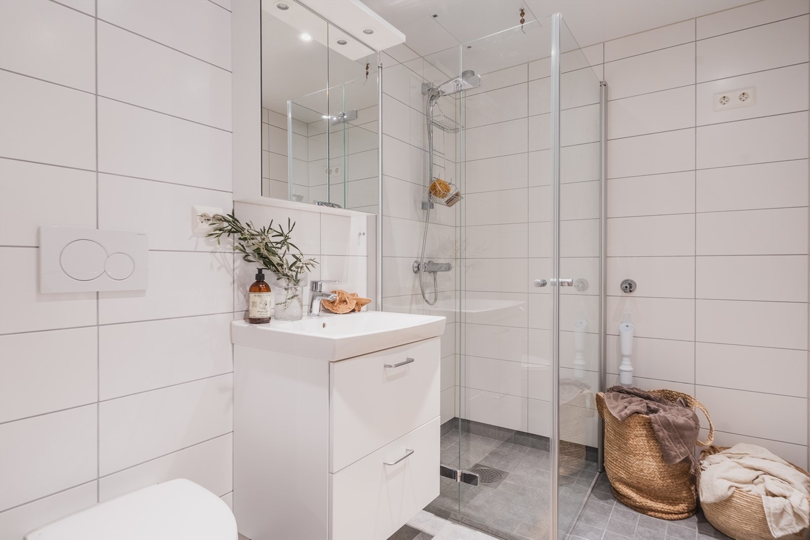 Baderommet er moderne og funksjonelt med delikate fliser på gulv og vegg. Veggmontert toalett og dusjløsning med glassdører gir et rent og luftig uttrykk. Galleribilde