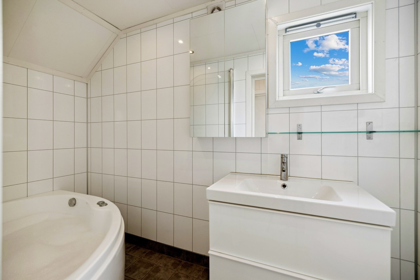 Badet har veggmontert toalett, servant i innredning med praktiske, store skuffer med demping, ettgreps armatur. Badekar i oval utførelse med boblebad, dusjgarnityr og dusjvegg i glass. Galleribilde