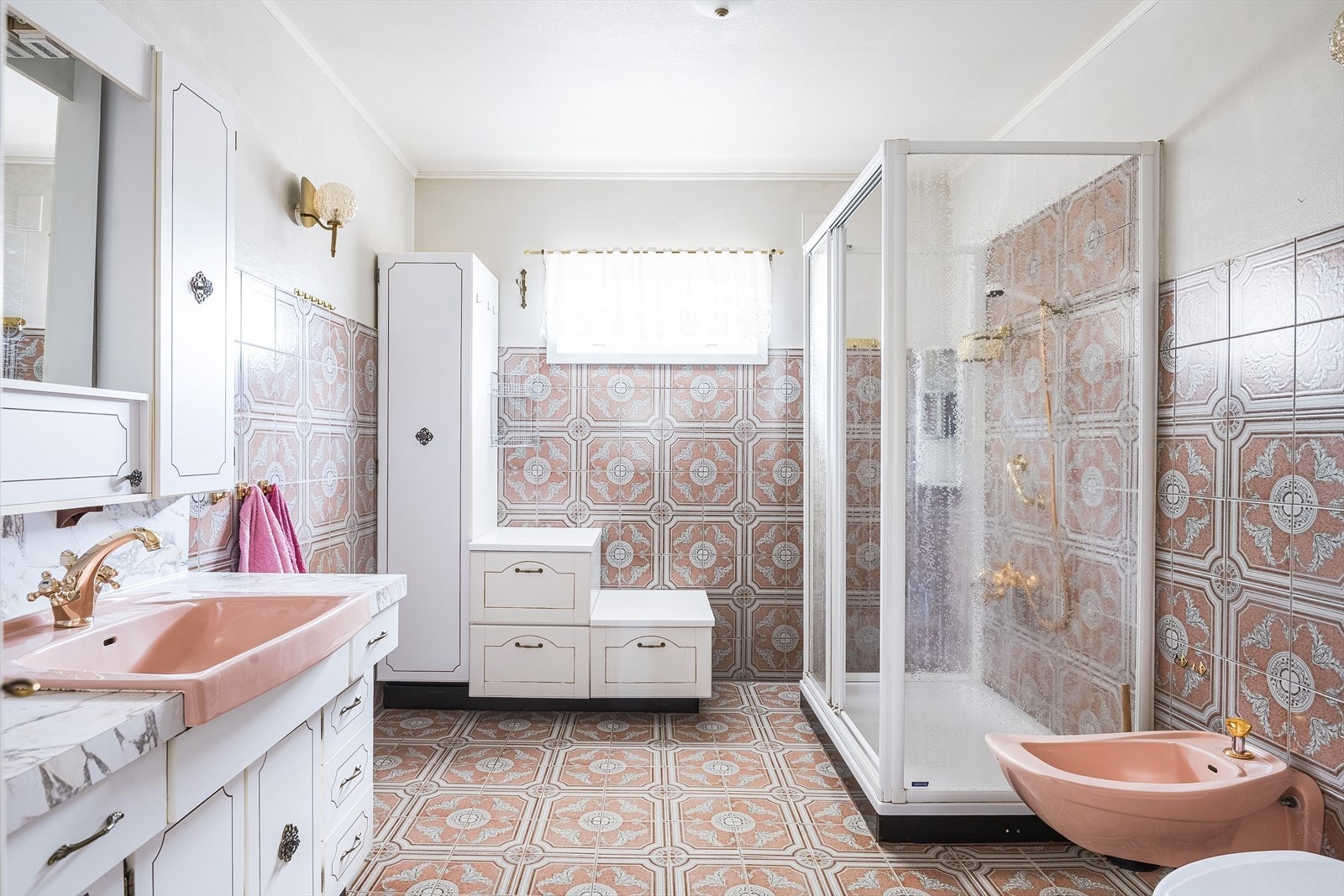 Stort eldre baderom med pene klassiske detaljer. Baderommet har nydelige fliser på gulv og vegger, baderomsinnredning med rosa servant, vegghengt toalett, rose bide, og romslig dusjkabinett. Galleribilde