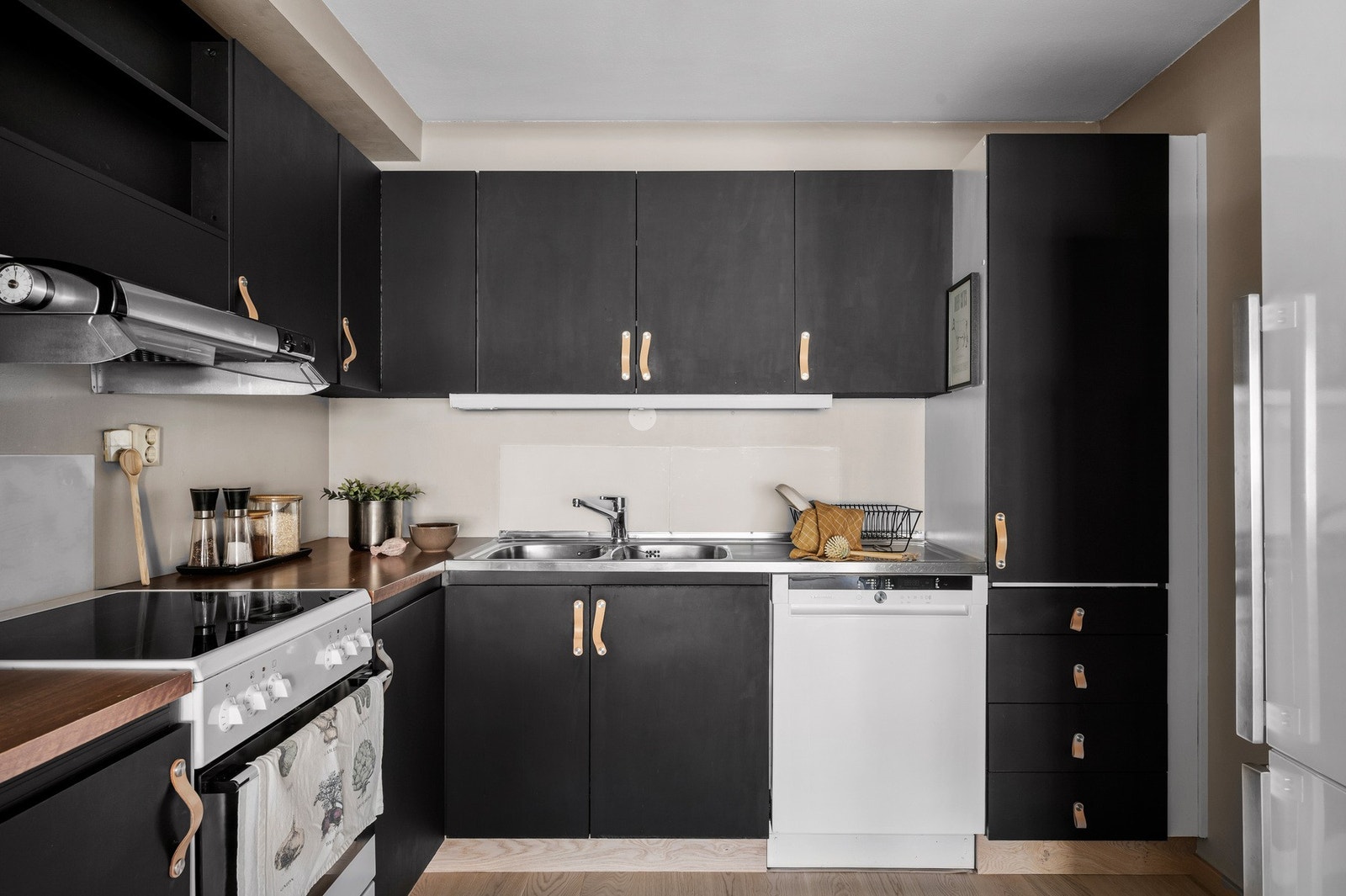 Kjøkkeninnredning med slette fronter, laminat benkeplate, over benkeplaten er det benyttet malte flater, stål oppvaskkum, ventilator. Galleribilde