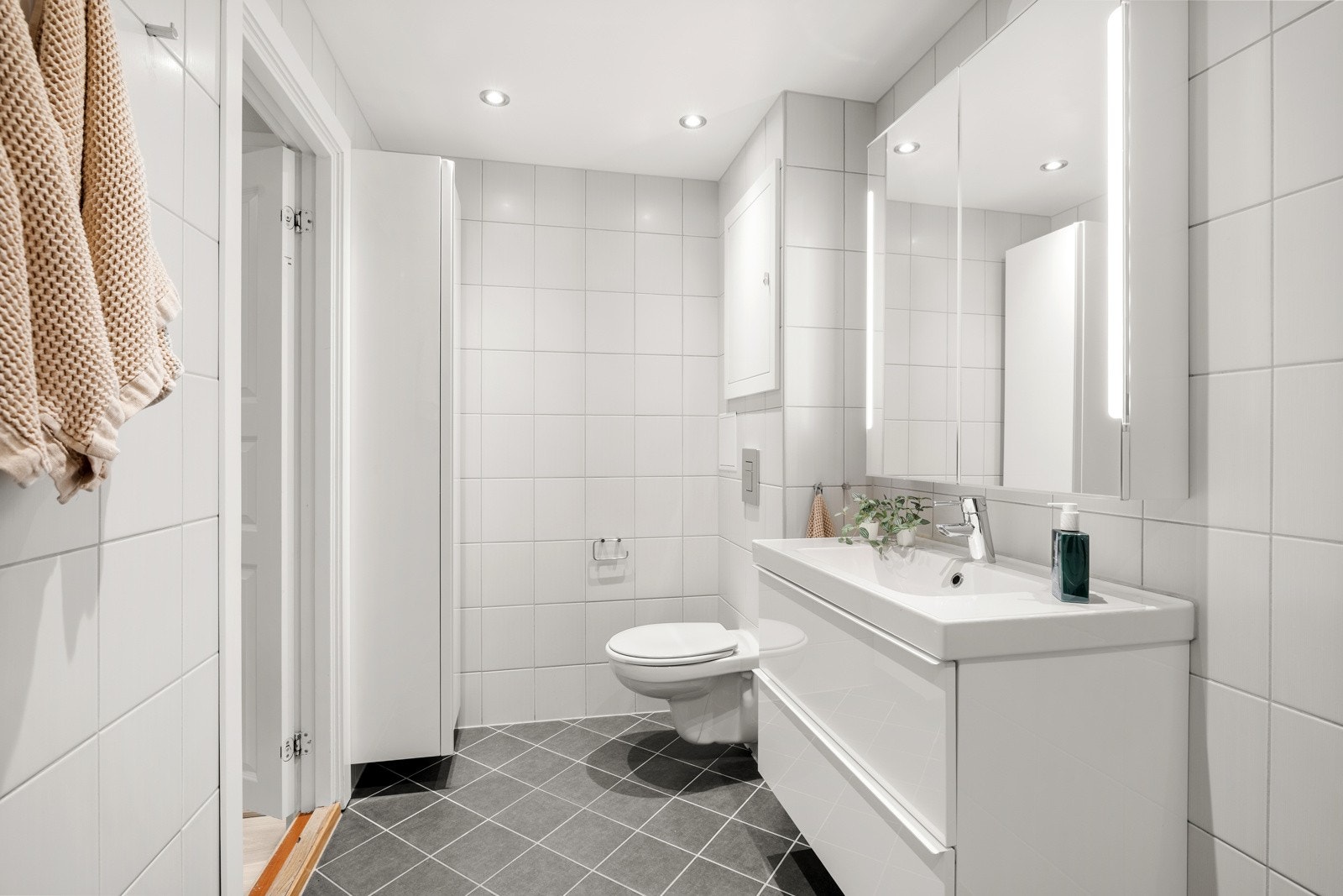 Baderomsinnredning med glatte hvite skuffefronter. Speilskap med integrert belysning over servant. Galleribilde