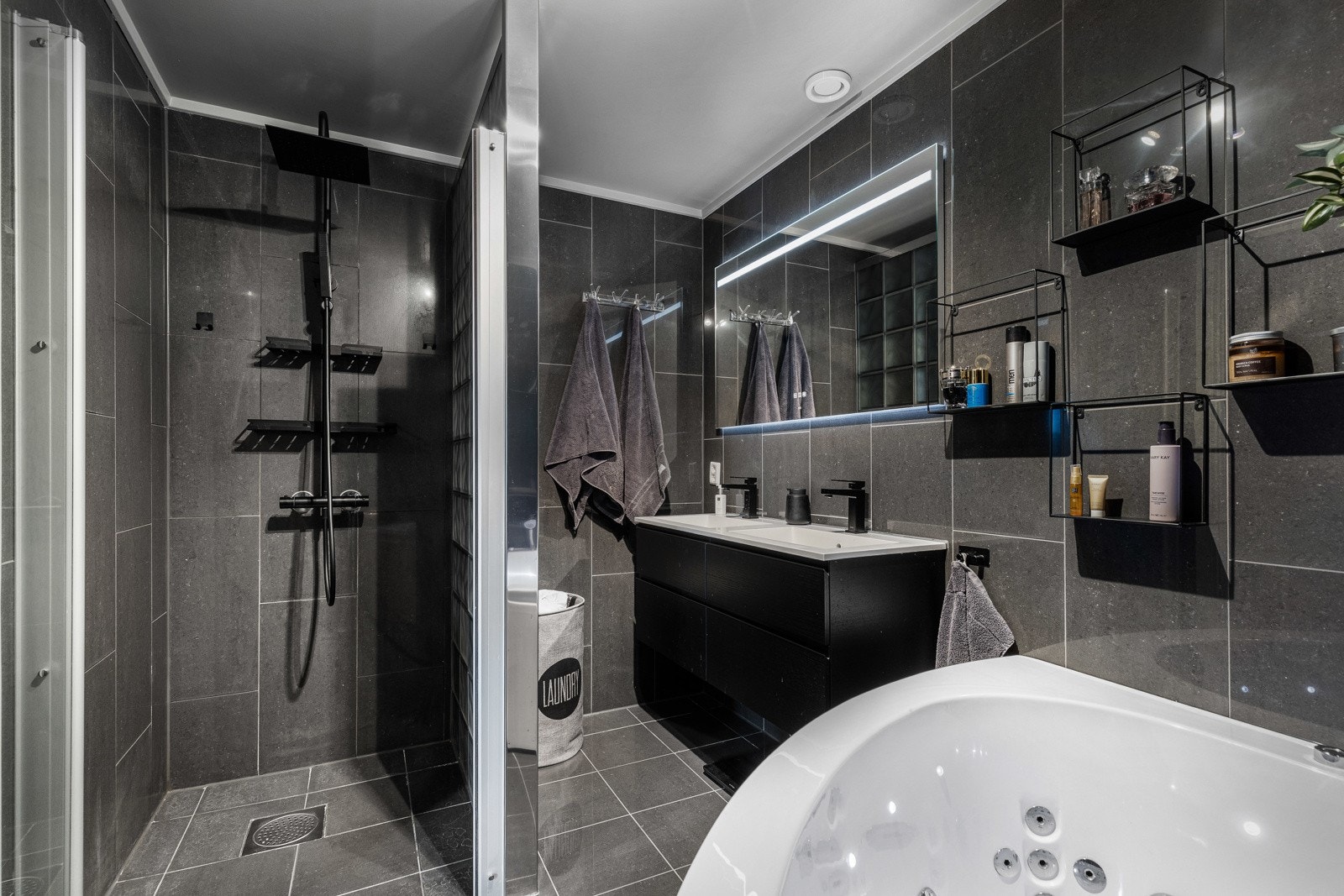 Moderne bad med dusjhjørne, dobbelt servant, stor speil med belysning og vegghengte hyller. Galleribilde