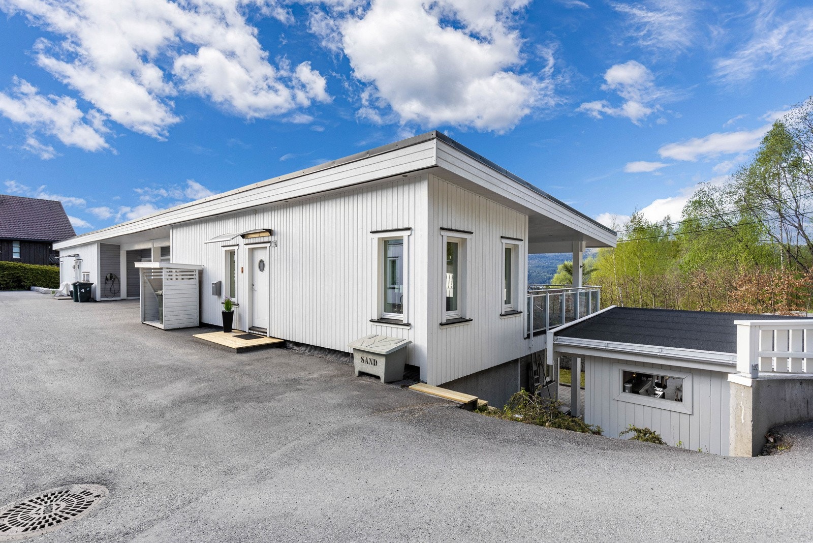 Hvit bolig med flatt tak og asfaltert innkjørsel, omringet av natur. Galleribilde