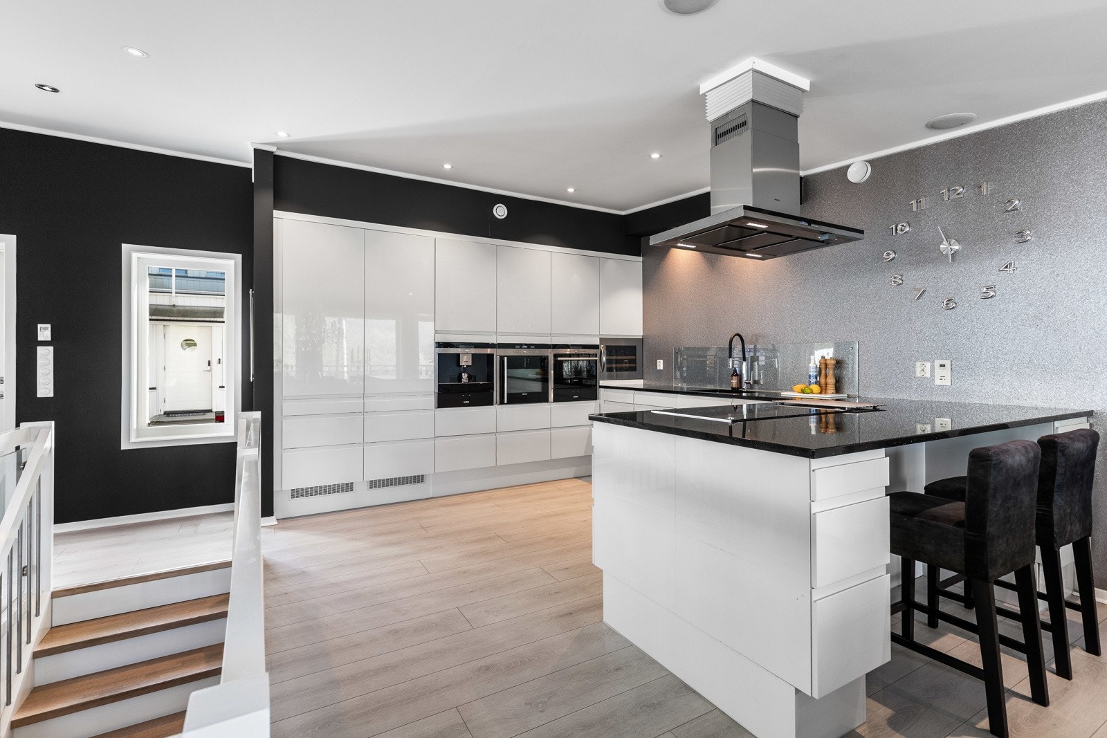 Moderne kjøkken med integrerte hvitevarer, kjøkkenøy og sitteplasser. Lyse gulv og kontrastvegger gir et stilfullt uttrykk. Galleribilde