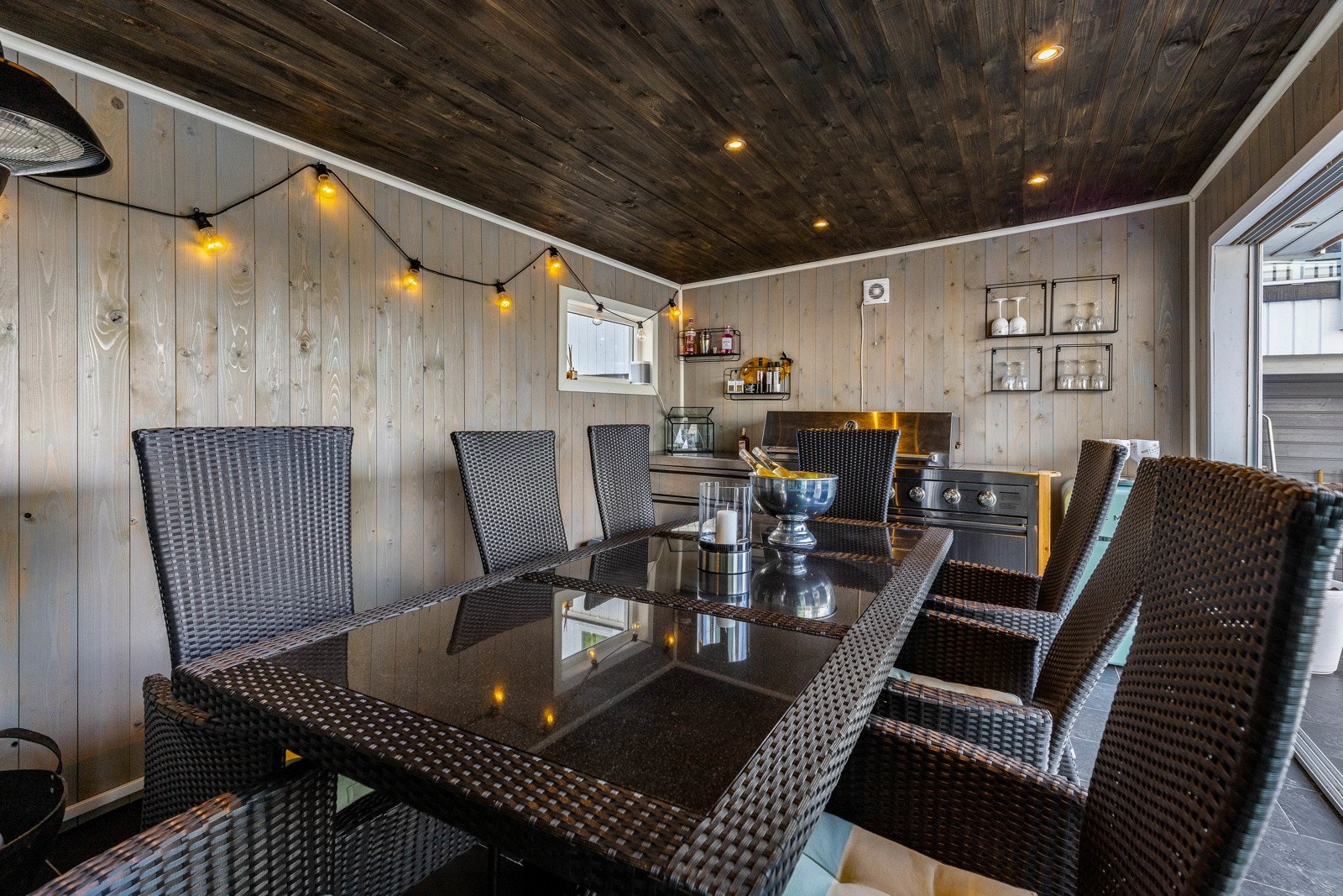 Romslig spiseplass med mørkt tretak og vegger, plass til langbord og stoler. Vegghyller og lyslenke gir ekstra hygge. Galleribilde