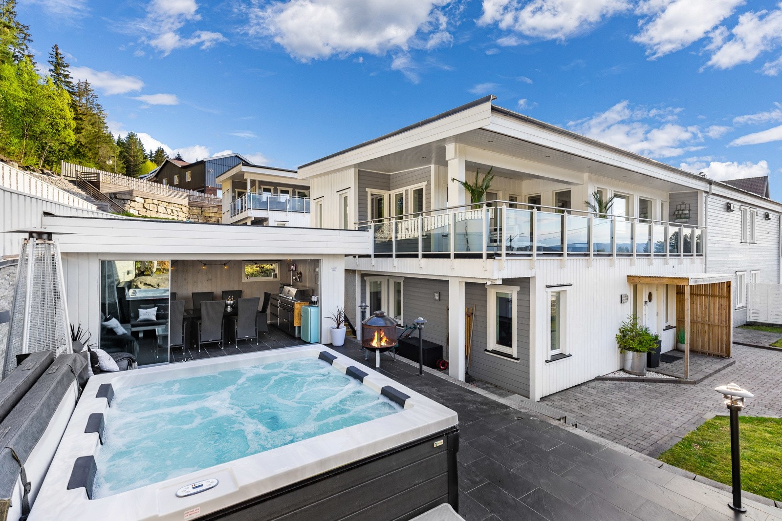 Moderne bolig med stor terrasse, boblebad (medfølger ikke) og utendørs spiseplass. Lyse fasader og pent opparbeidet uteområde med steinbelagte gangveier. Galleribilde