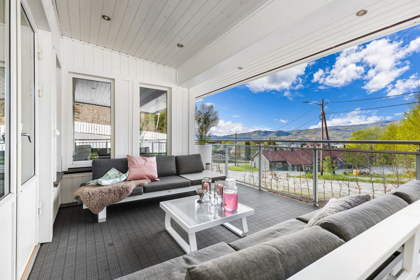 Overbygd balkong med utsikt mot åser og boligområde. Store vinduer og glassrekkverk gir lys og luft. Galleribilde