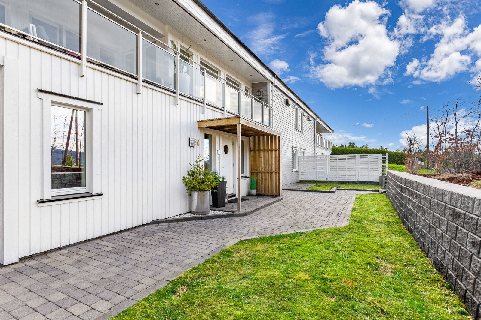 Moderne, hvitmalt fasade med stor balkong og inngangsparti. Steinlagt gangvei og velholdt plen. Galleribilde