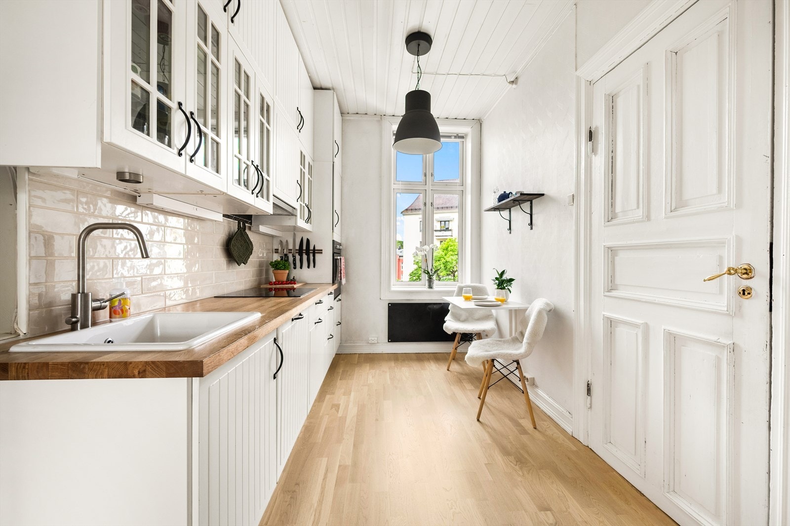 Lys og klassisk innredning fra 2006 med profilerte fronter (malt i 2020), fliser på vegg over kjøkkenbenk og heltre benkeplate. Galleribilde