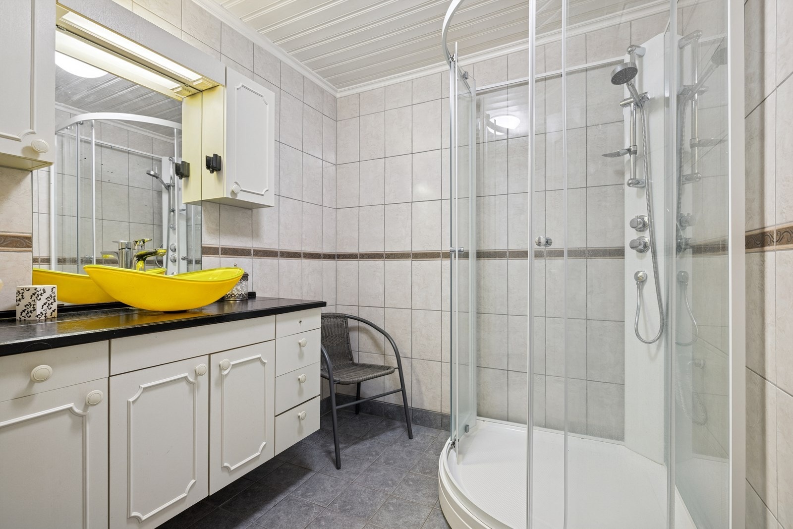 Baderomsinnredningen er pent utført med hvite profilerte fronter, med skuffer og skap, og benkeplate med servant. Galleribilde