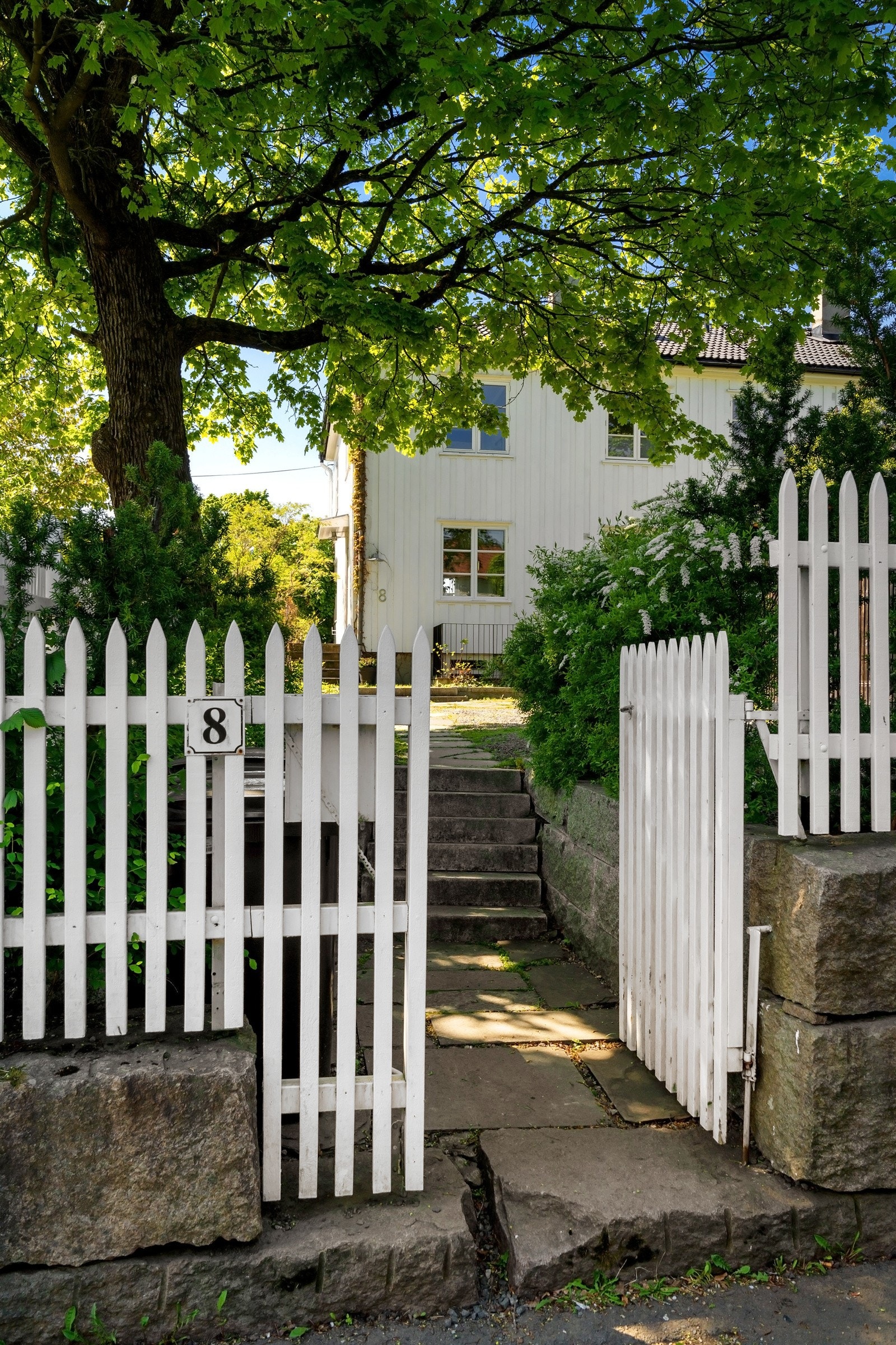 Frodig hekk og hvitmalt stakitt markerer skillet mot veien og naboeiendommene. Galleribilde