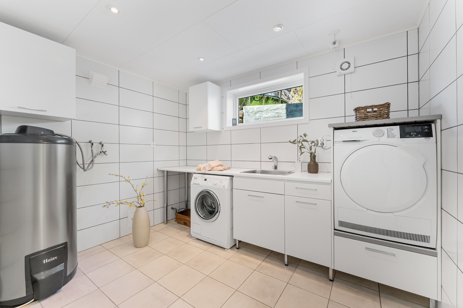 Vaskerom med nedfelt servant og opplegg for vaskemaskin og tørketrommel. Her er varmtvannstank som er fra 2017. Galleribilde