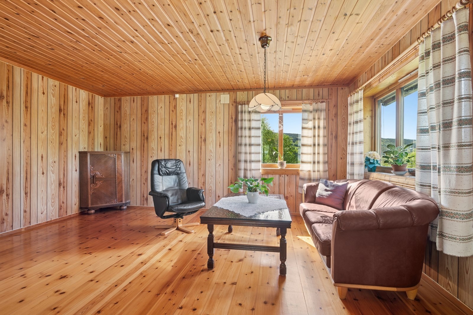 En romslig stue med heltre furugulv og store vinduer som slipper inn mye naturlig lys. Galleribilde