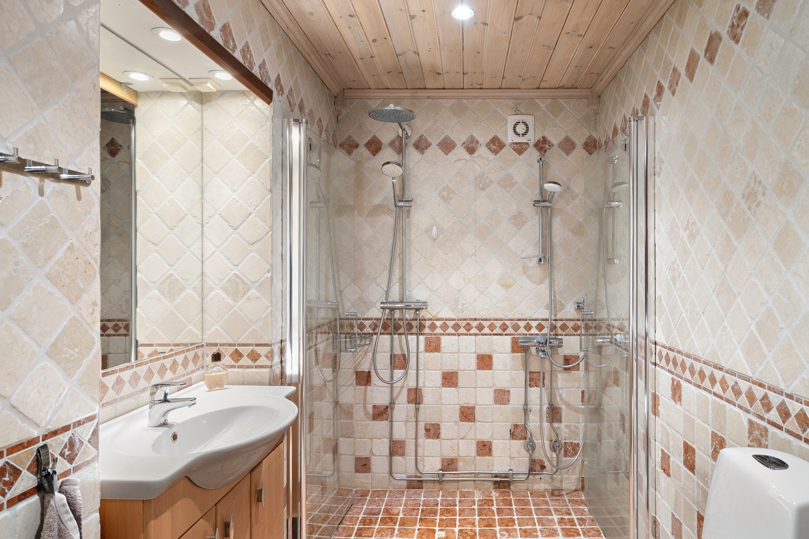 Flislagt baderom med varmekabler. Rommet er innredet med dobbel dusjløsning, servant med underskap, toalett og opplegg for vaskemaskin og tørketrommel Galleribilde