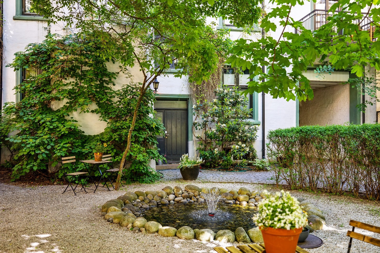 Bakgård med vannfontene, steinbord, flere sitteområder og sykkelparkering. Galleribilde