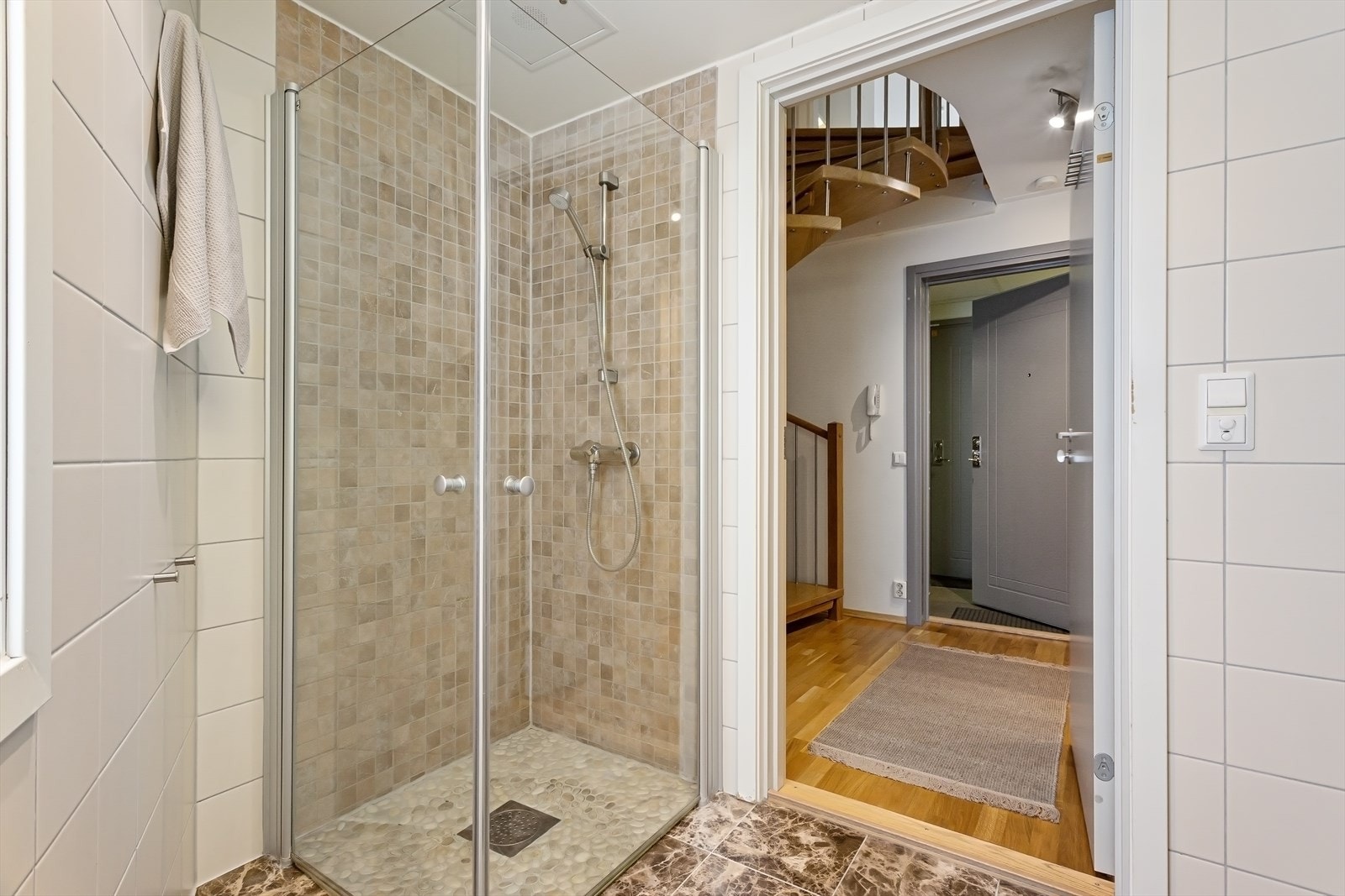 Badet er innredet med veggmontert toalett, dusjhjørne med innfellbare glassdører og baderomsinnredning med skuffer, servant og speil med belysning. Galleribilde