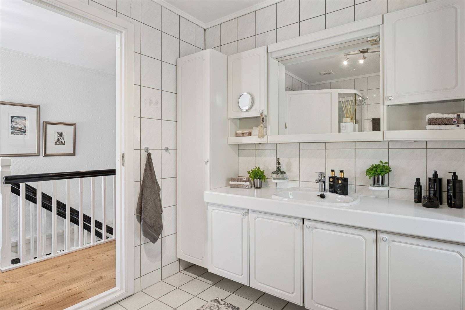 Rommet er innredet med en stor baderomsinnredning med skapseksjoner og nedfelt servant, belyst speil, dusjkabinett og toalett. Badet fremstår som lyst og delikat. Galleribilde