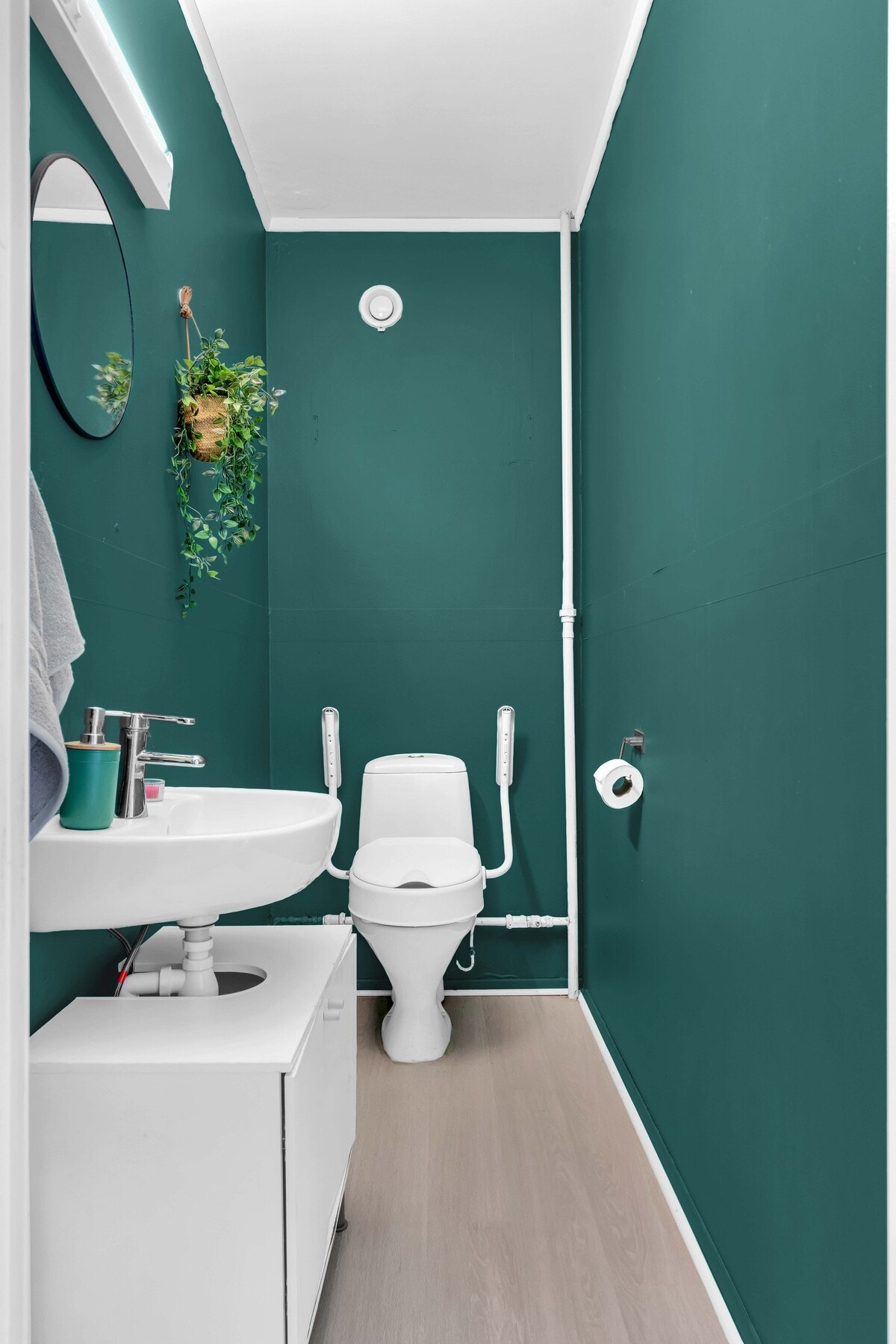 Praktisk separat toalettrom med gulvstående servantskap, vegghengt servant, speil med overbelysning og frittstående toalett. Galleribilde